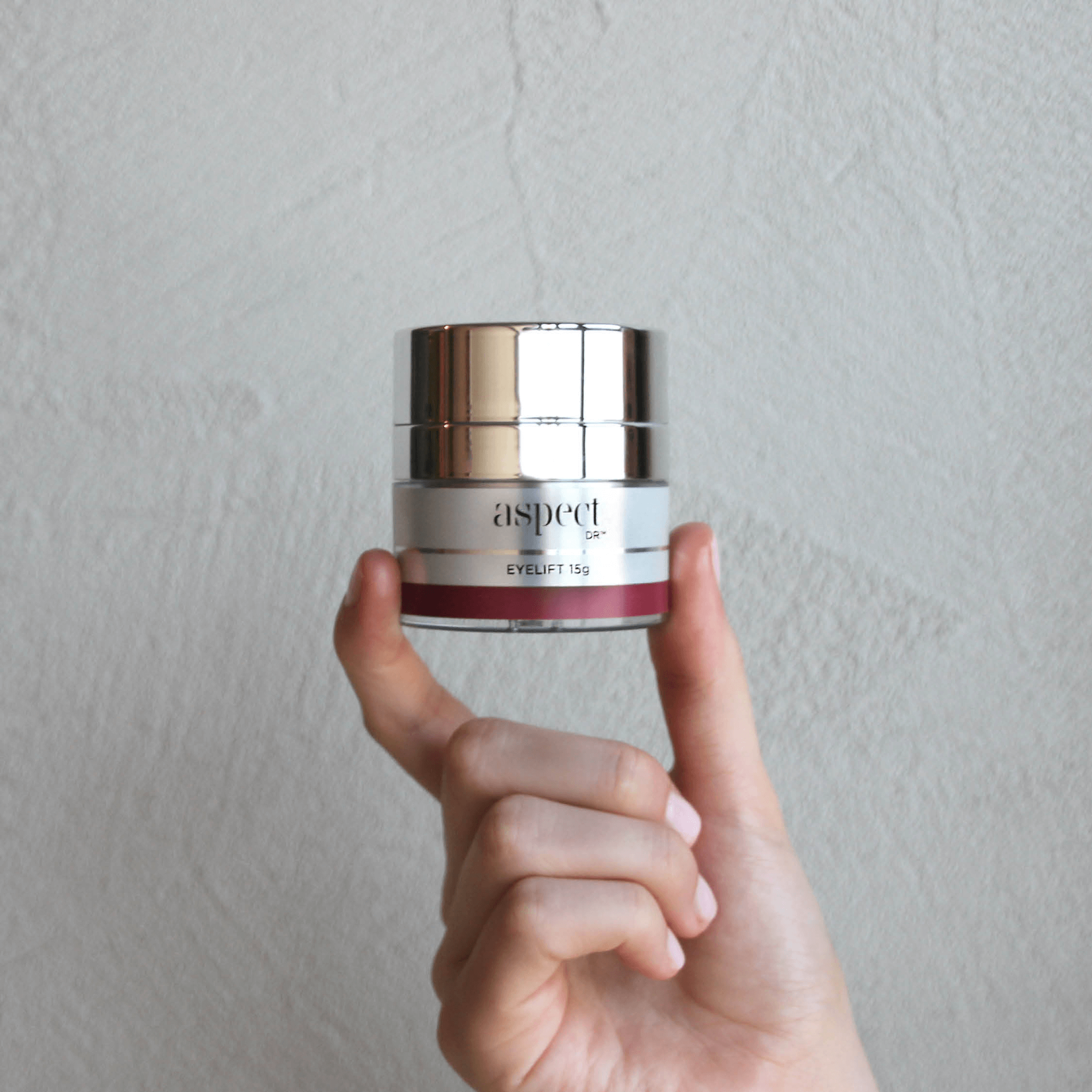 Aspect Eye Lift 15g jar being held near a textured background