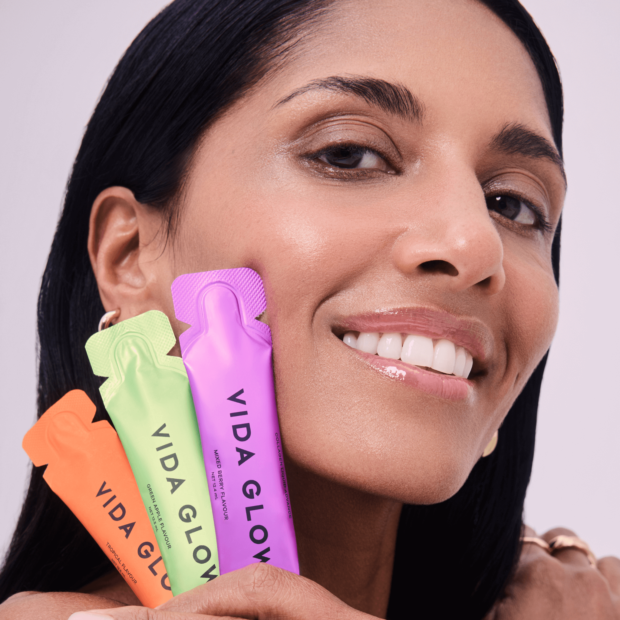 Woman holding Vida Glow liquid sachets against a neutral background