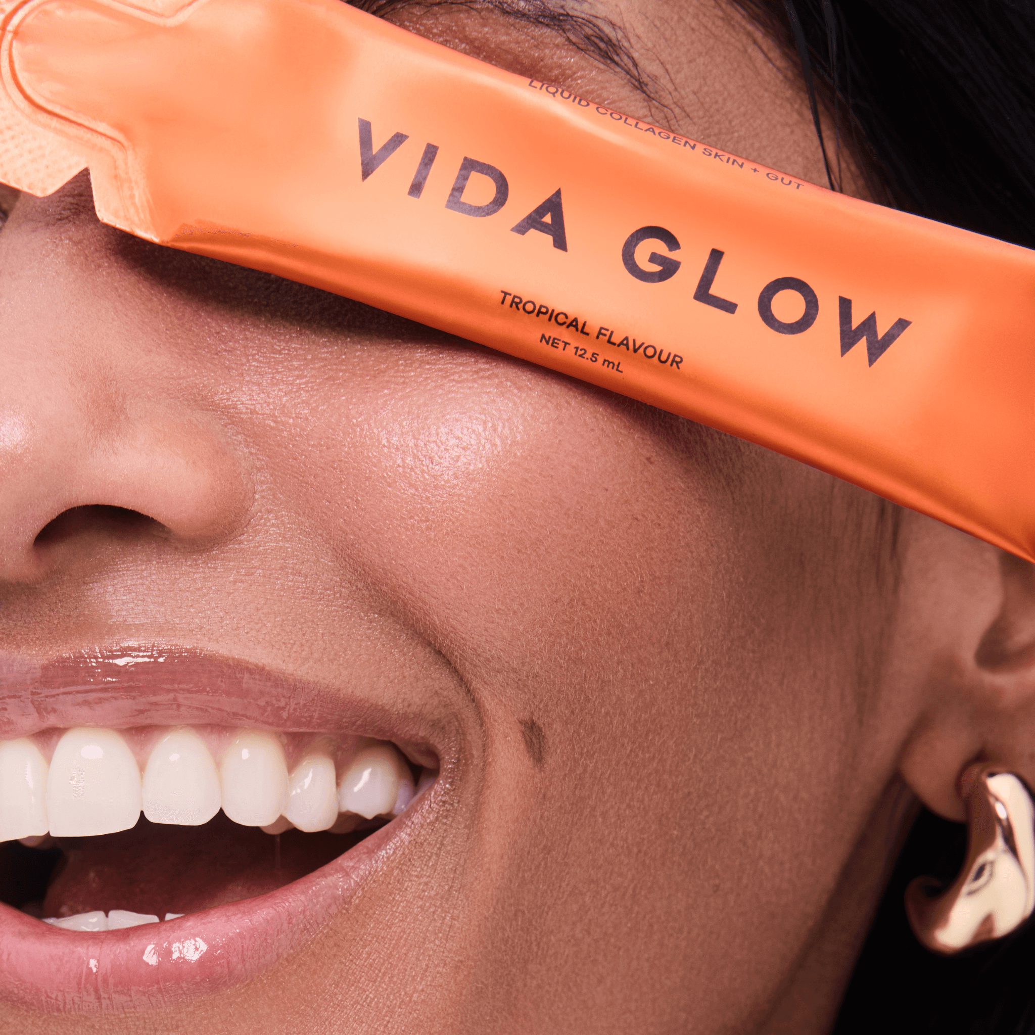 Person holding an orange 'Vida Glow' tropical flavour 12.5ml sachet close to their face