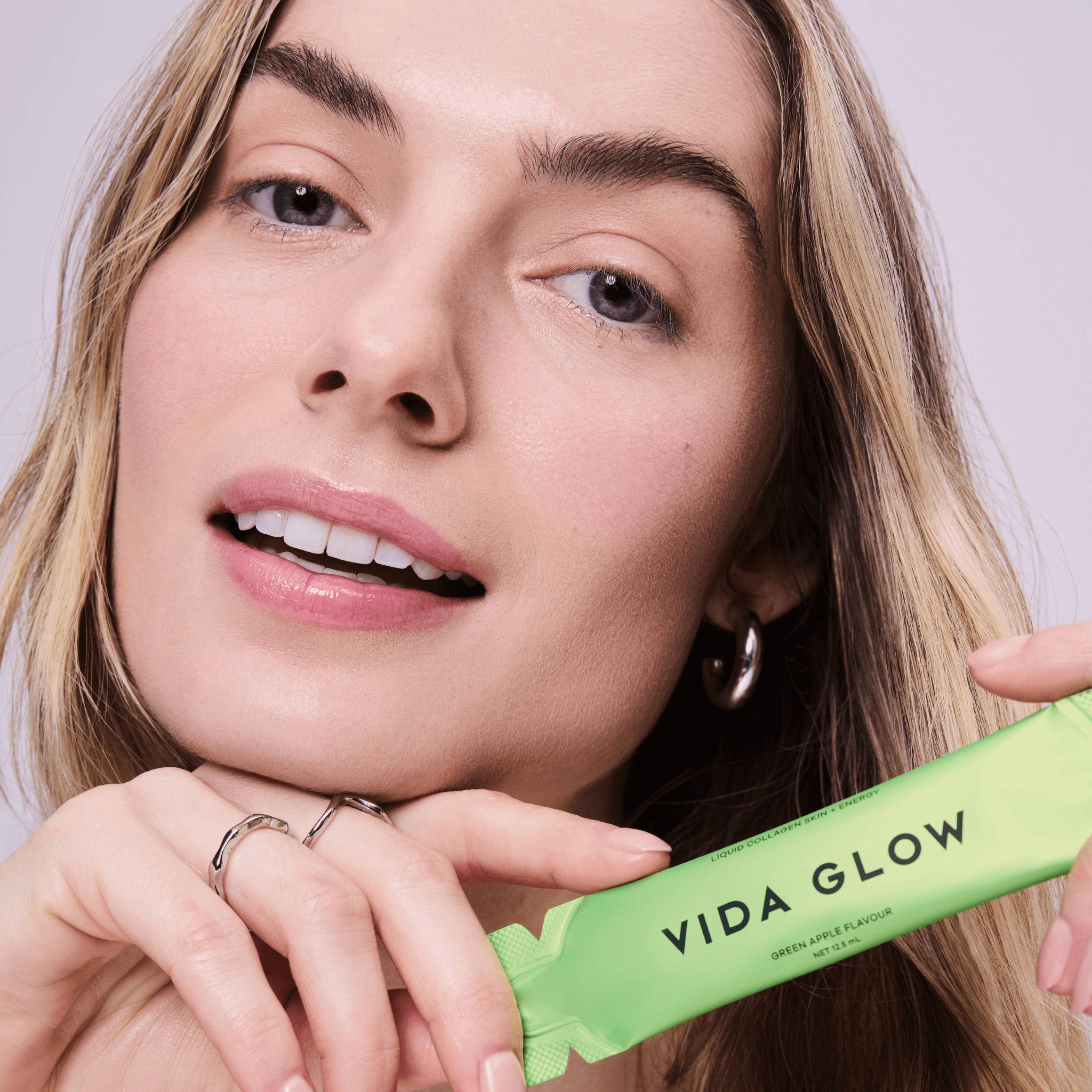 Woman holding a green Vida Glow liquid collagen sachet against a neutral background