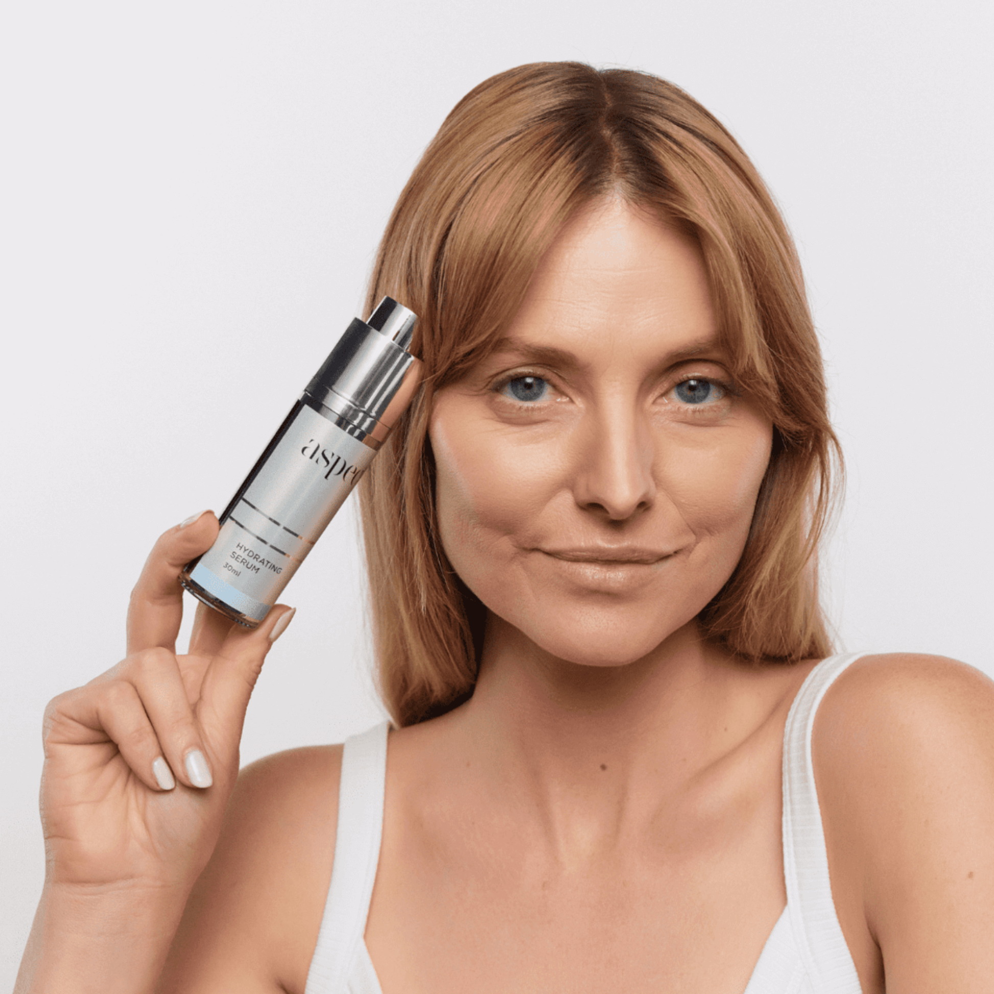 Woman holding an Aspect Hydrating Serum skincare bottle with a plain background