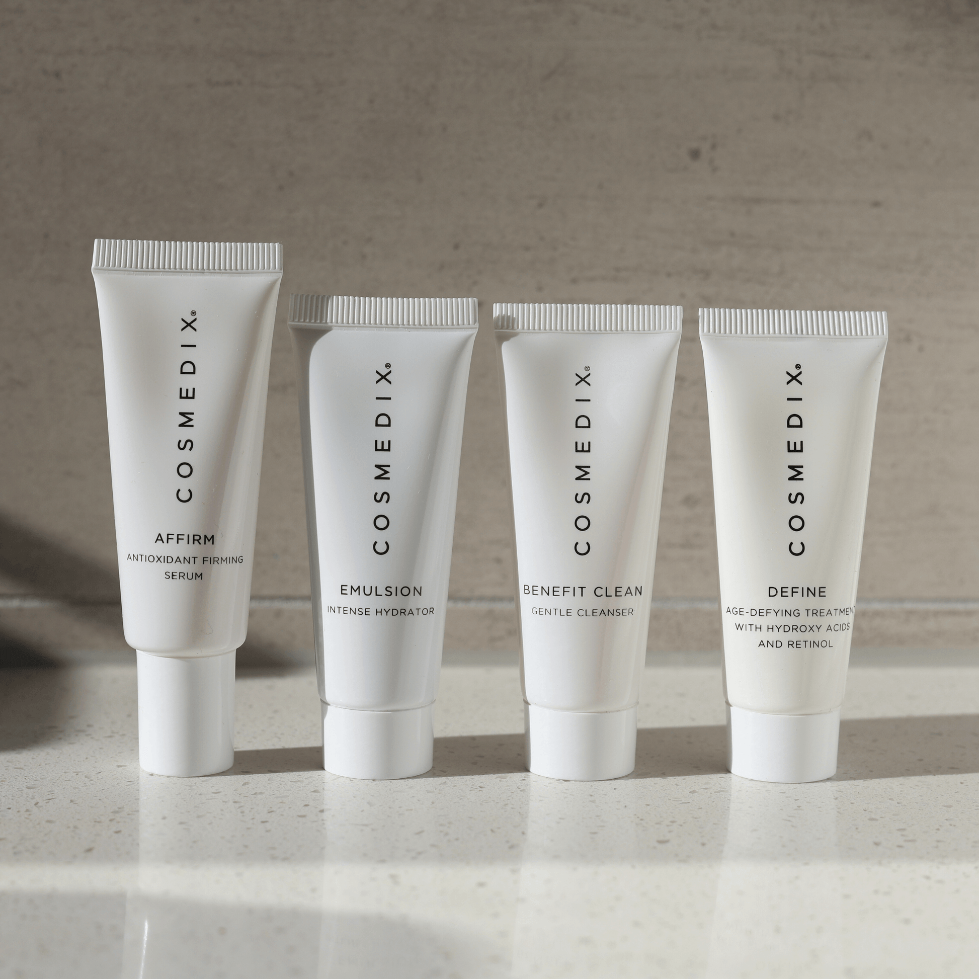 Four Cosmedix skincare products "Affirm, Emulsion, Benefit Clean, Define' on a neutral background