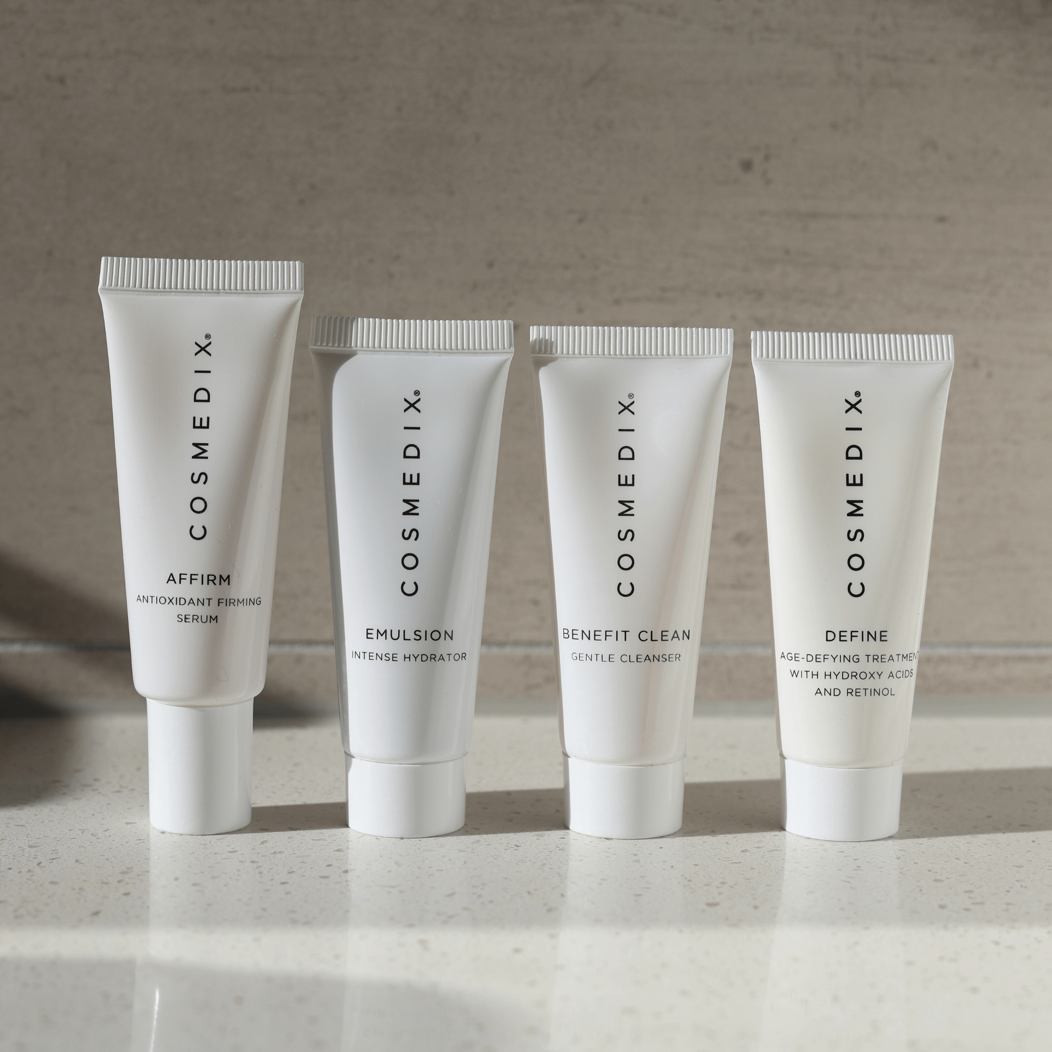 Four Cosmedix skincare products "Affirm, Emulsion, Benefit Clean, Define' on a neutral background