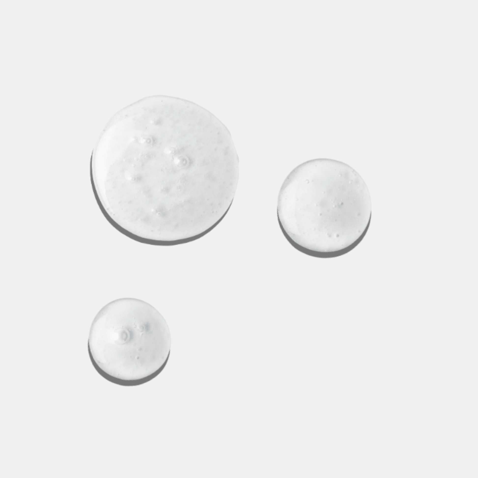 Three droplets of a white cream from Aspect Clear Skin Set on a light grey background
