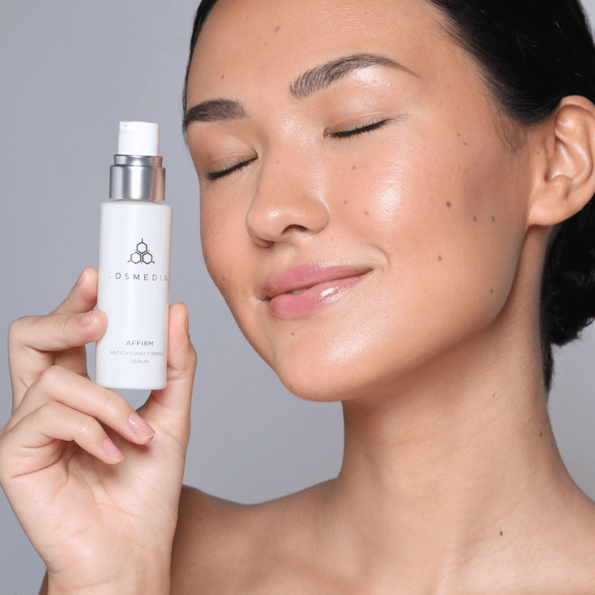 Woman holding Cosmedix Affirm bottle on grey background