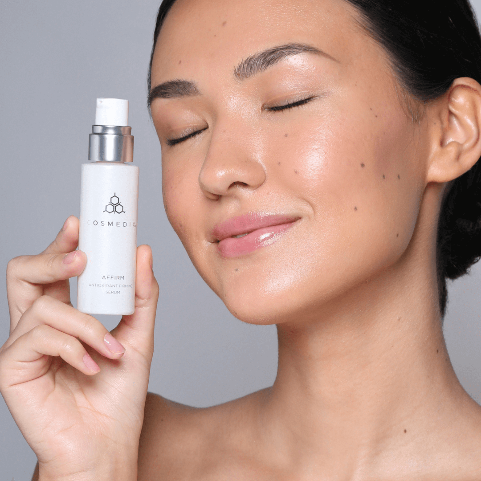 Woman holding Cosmedix Affirm bottle on grey background