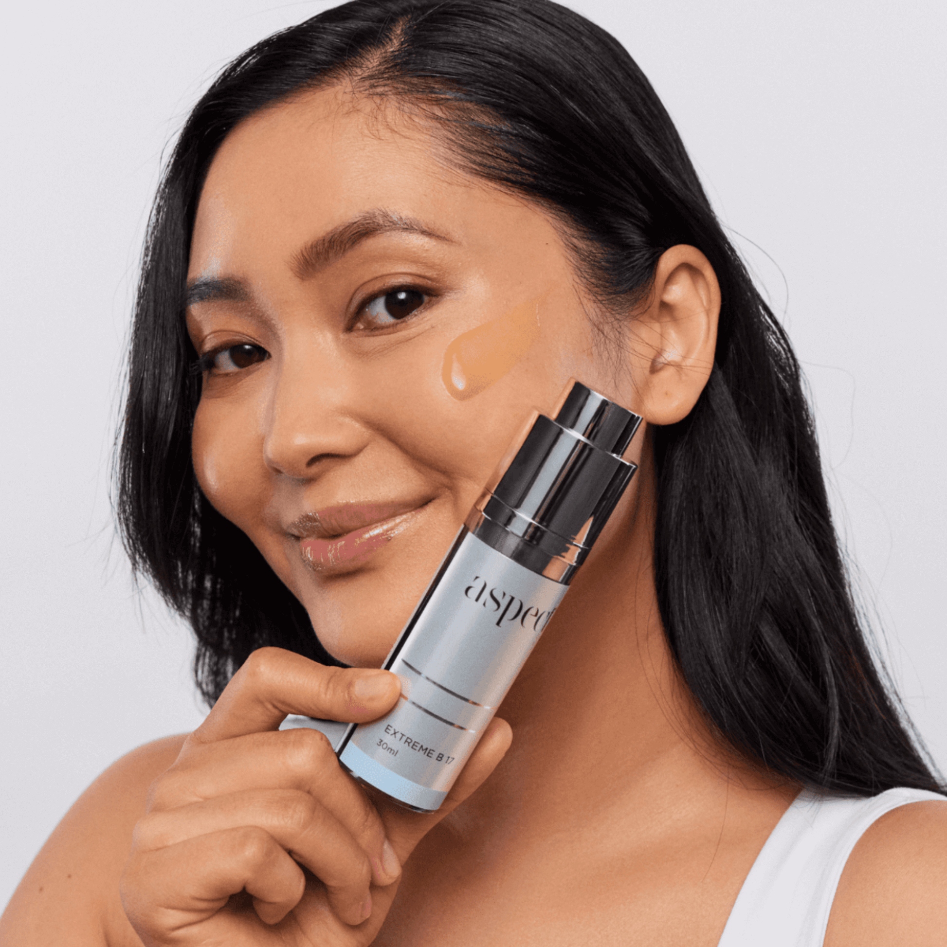 Woman applying Aspect B 17 product to face on a light grey background 