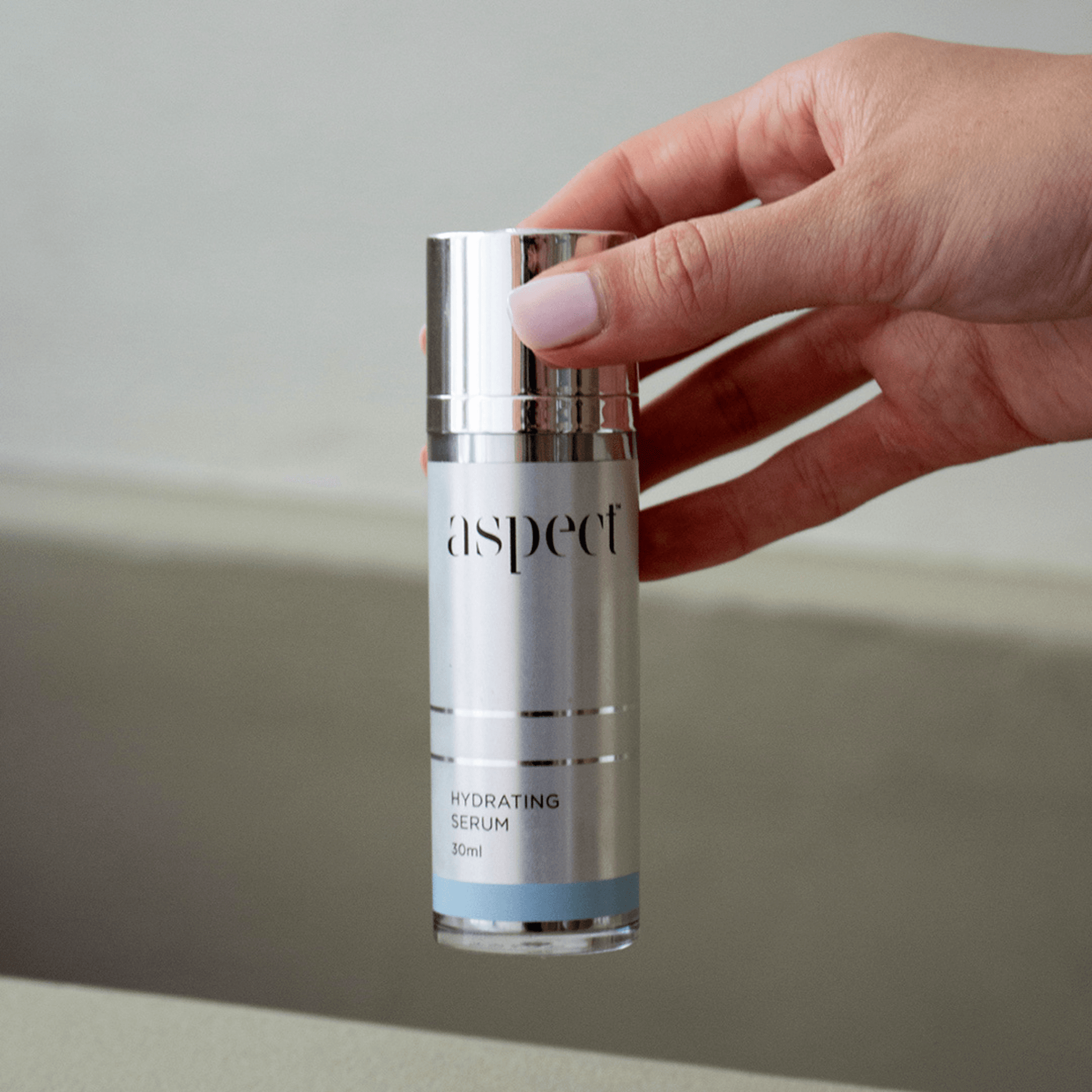 Hand holding a skincare serum bottle labeled 'aspect hydrating serum' against a neutral background
