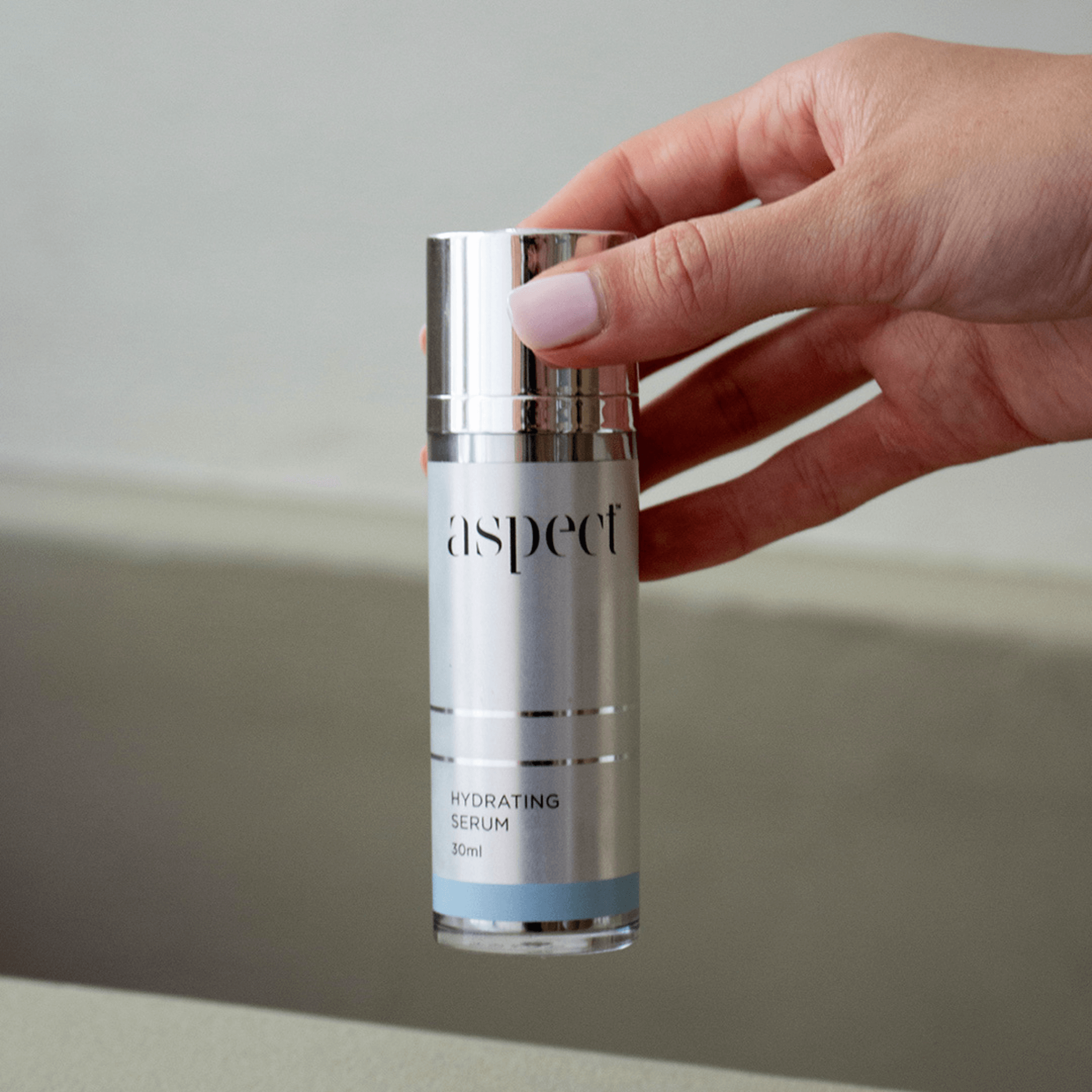 Hand holding a skincare serum bottle labeled 'aspect hydrating serum' against a neutral background