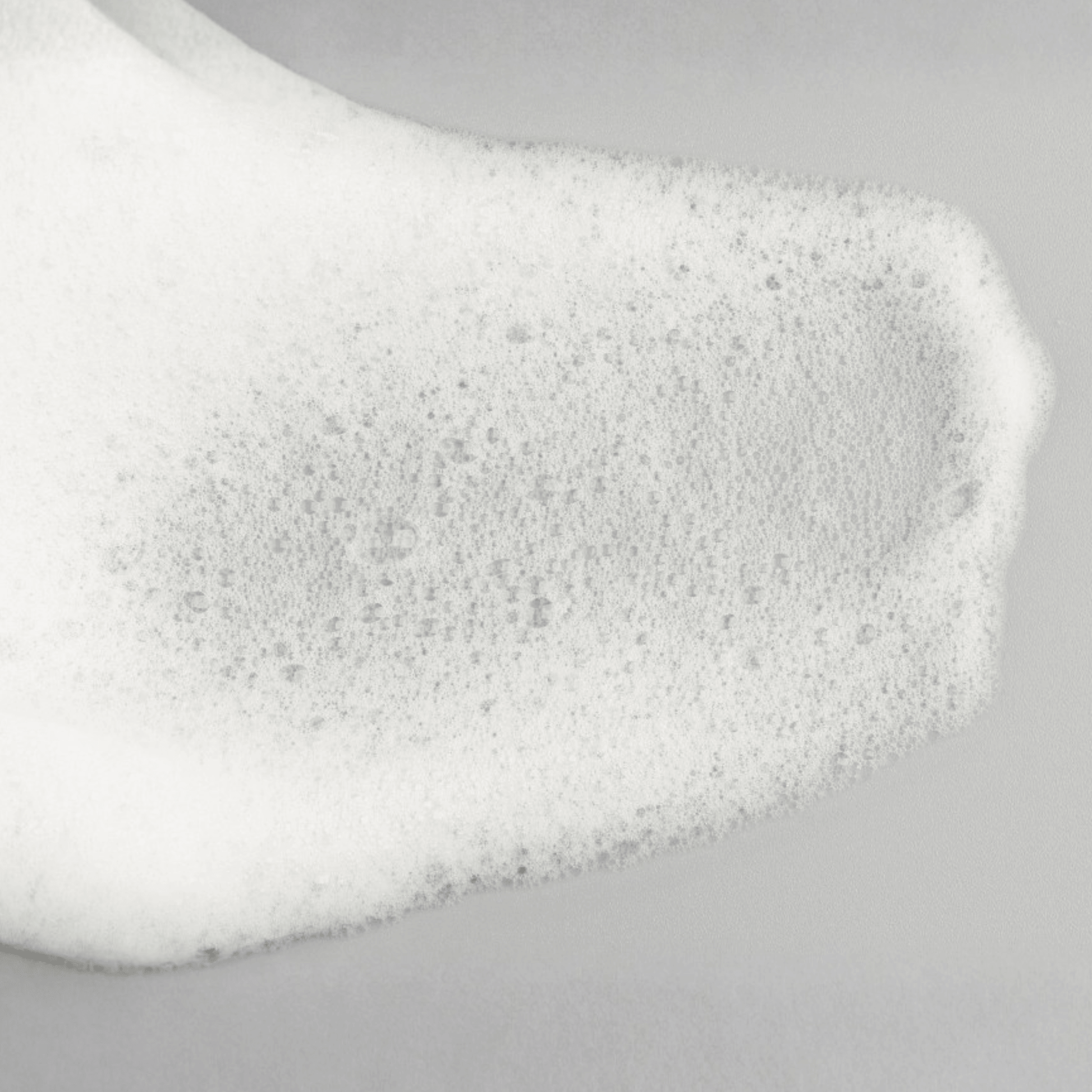 Close-up of Aspect Dr AHS/BHA cleanser foam with dense bubbles on a light grey background