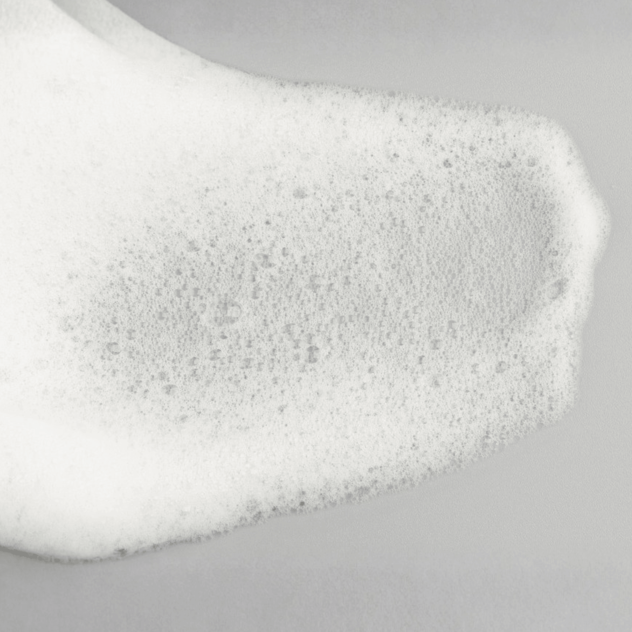 Close-up of Aspect Dr AHS/BHA cleanser foam with dense bubbles on a light grey background