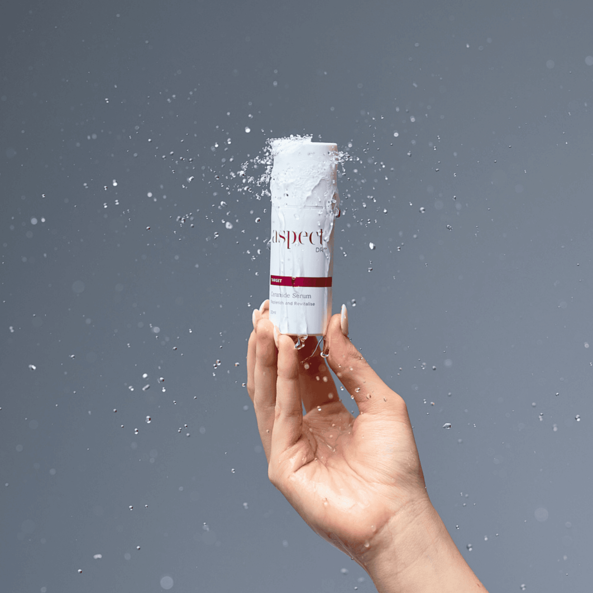 Aspect Dr Ceramide serum splashed with water handheld on grey background