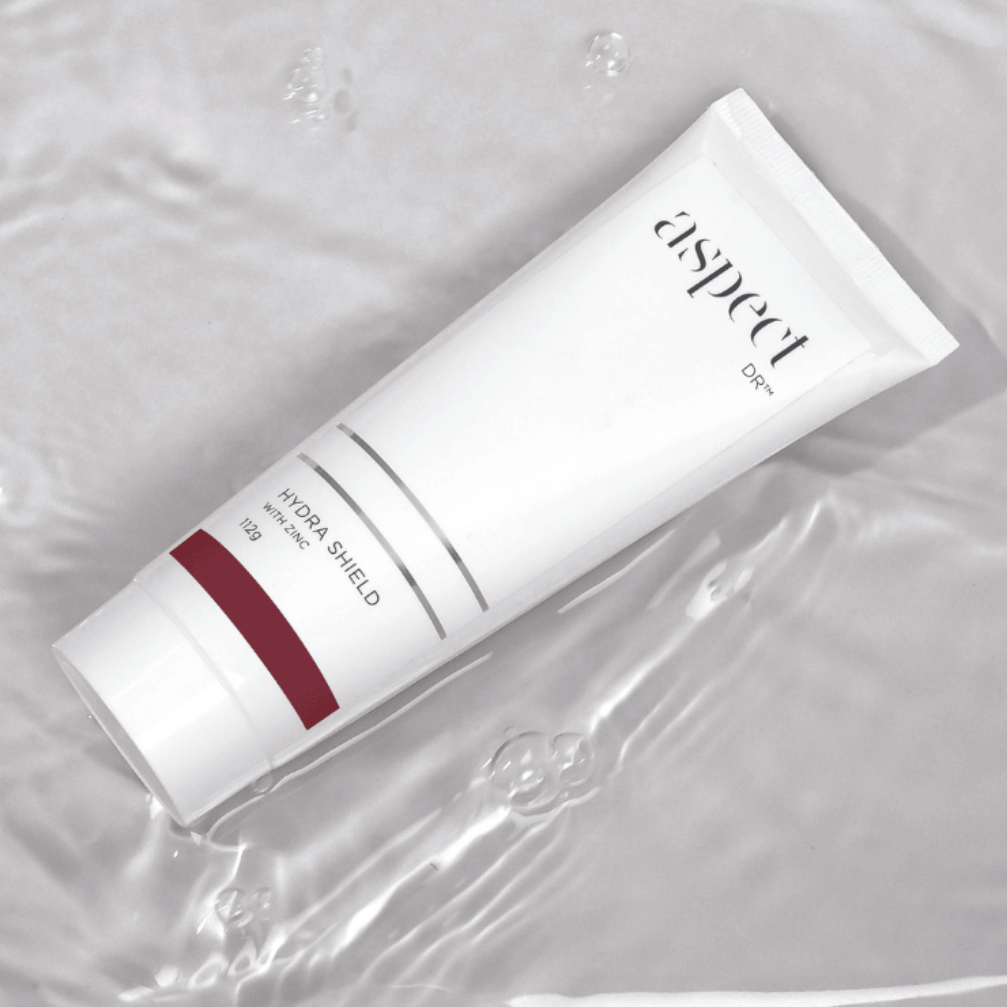 A white cosmetic tube of Aspect Dr Hydra Shield with Zinc on a glossy, water-like reflective surface