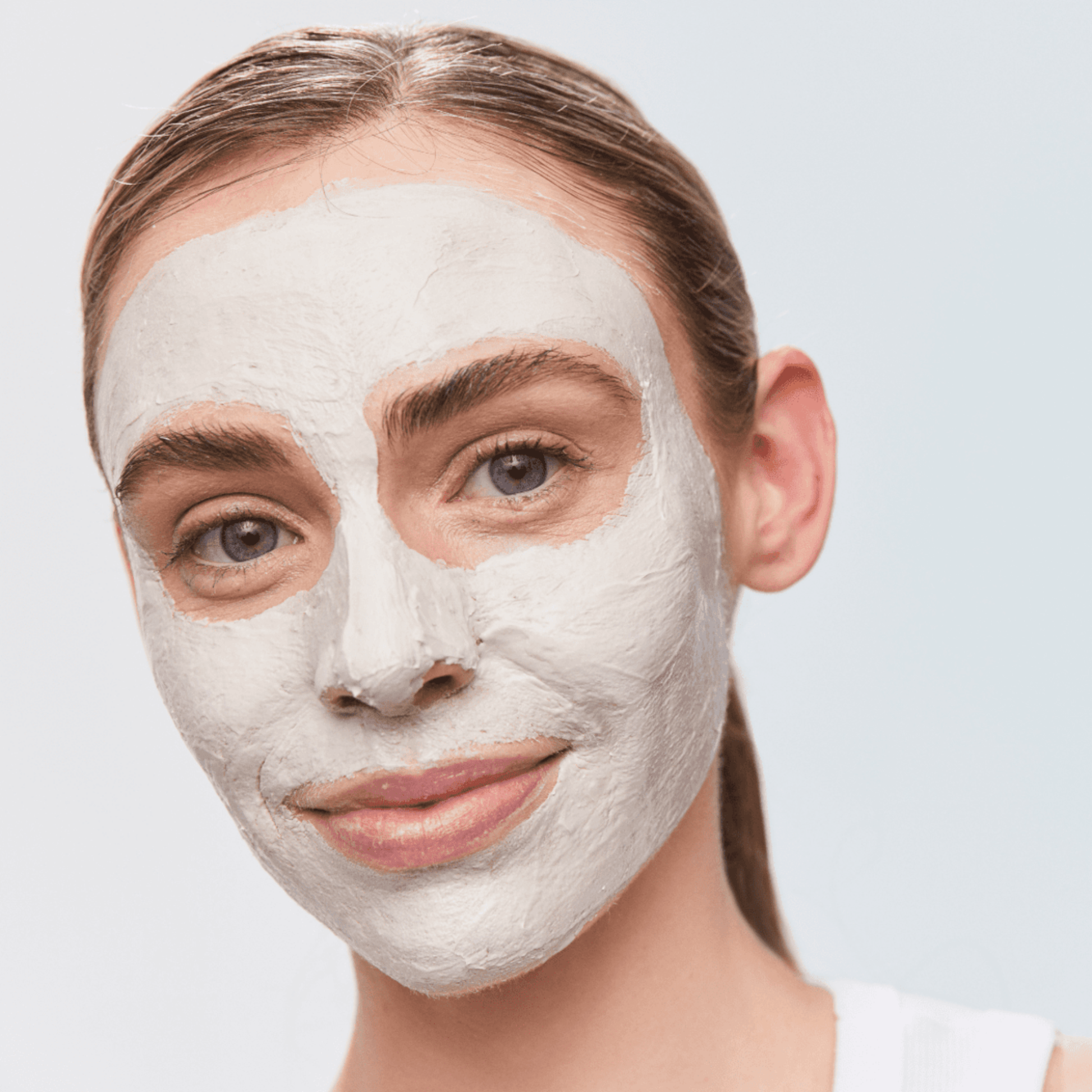 Woman with a light grey facial mask wearing Aspect Exfoliating Clay Mask on a plain background