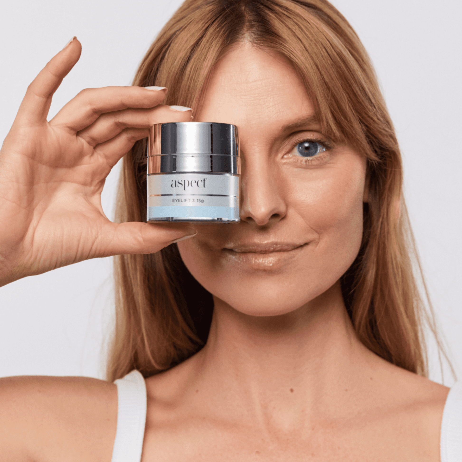 Woman holding a jar of Aspect Eye lift skincare product in front of her eye