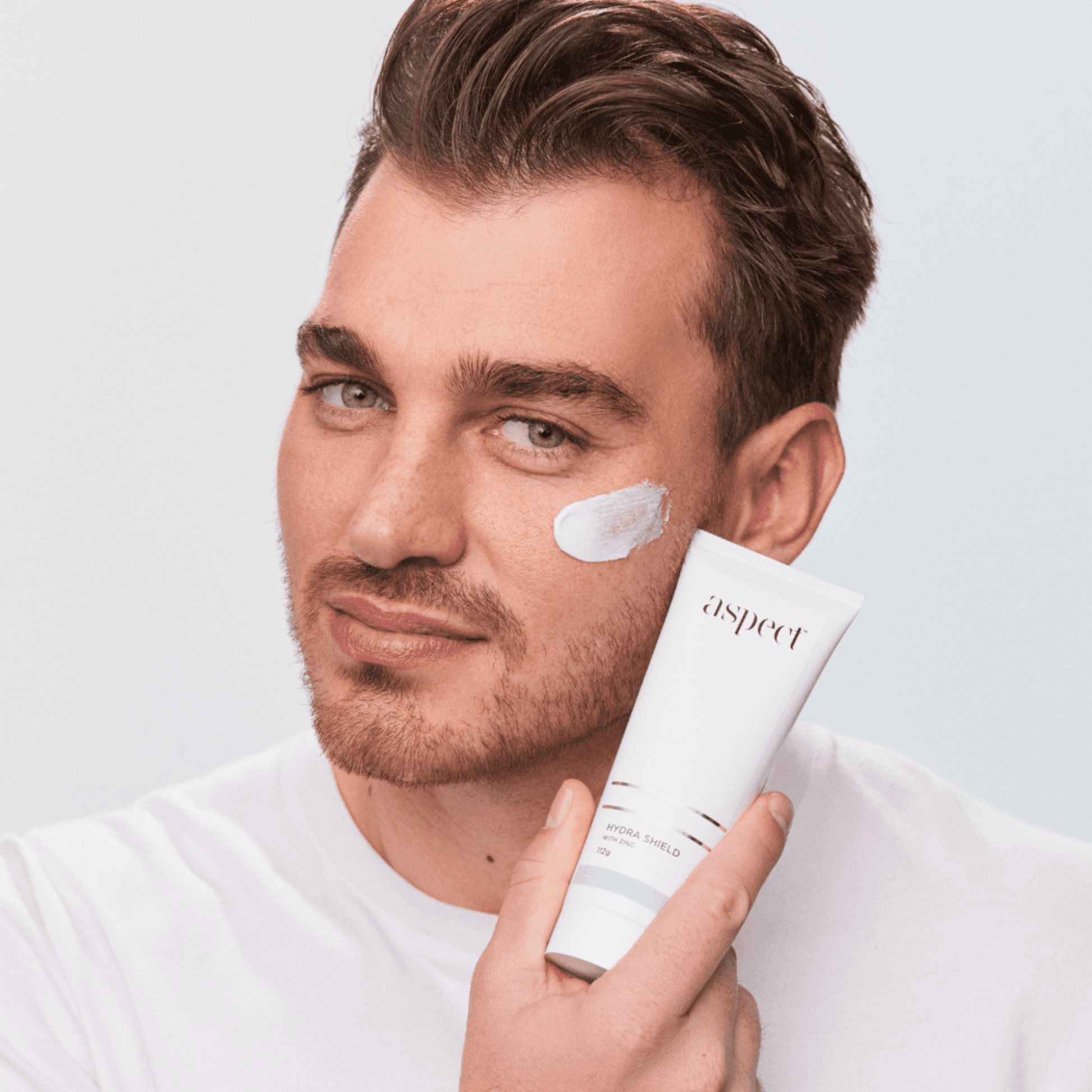 Man applying Aspect Hydra Shield to his face with a light grey background