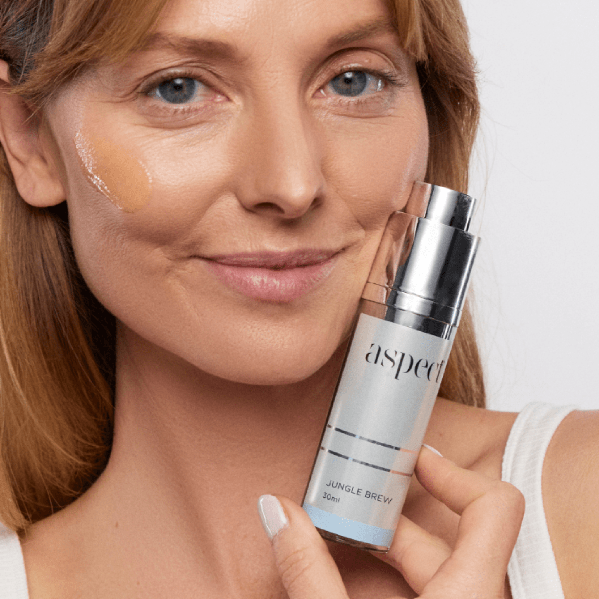 Woman holding Aspect Jungle Brew serum bottle on a plain background