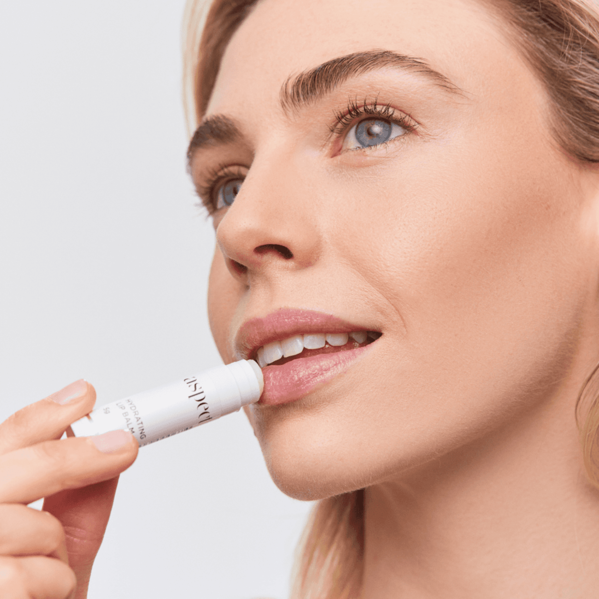 Woman applying Aspect lip balm with a neutral background