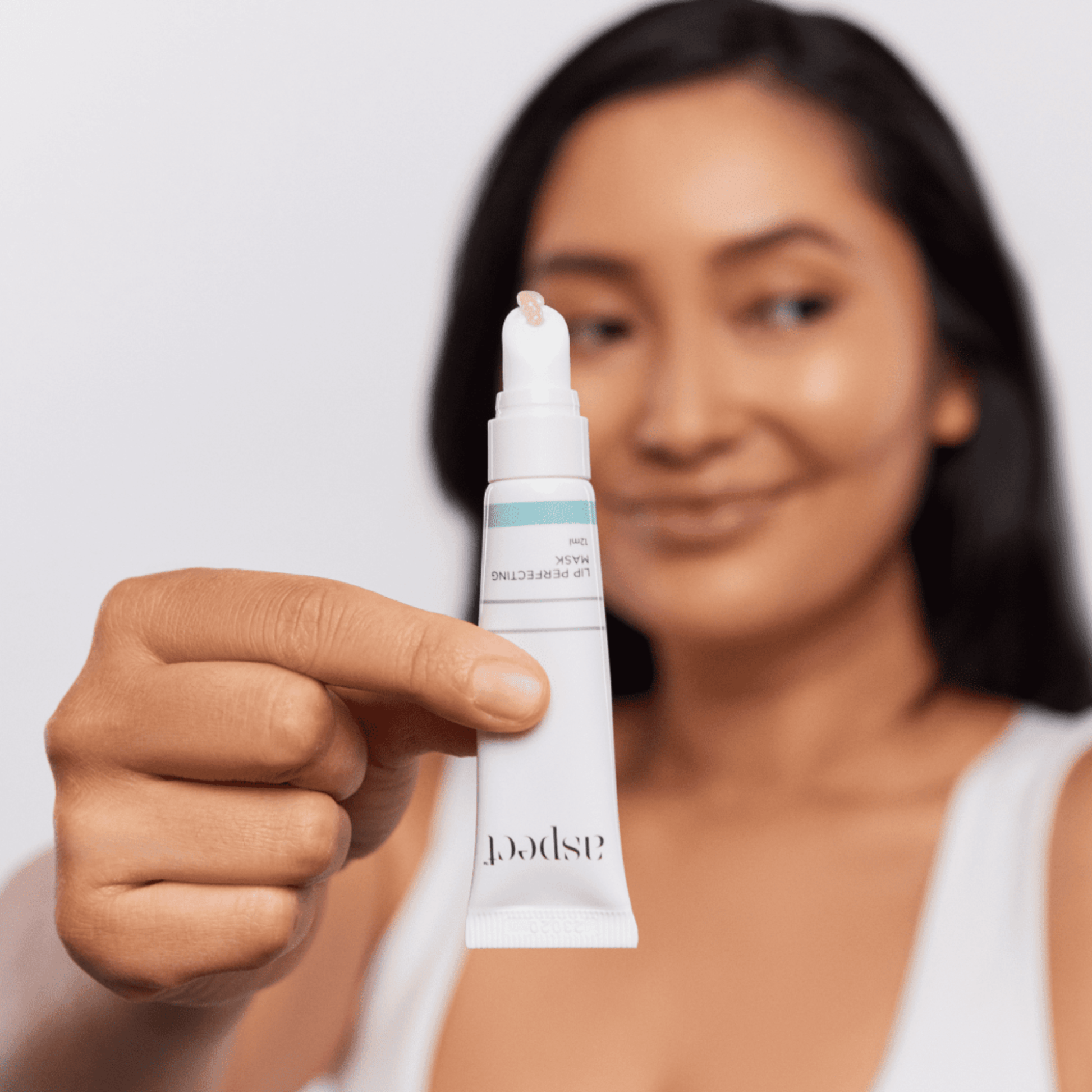Woman holding an Aspect Lip Mask tube with a plain background