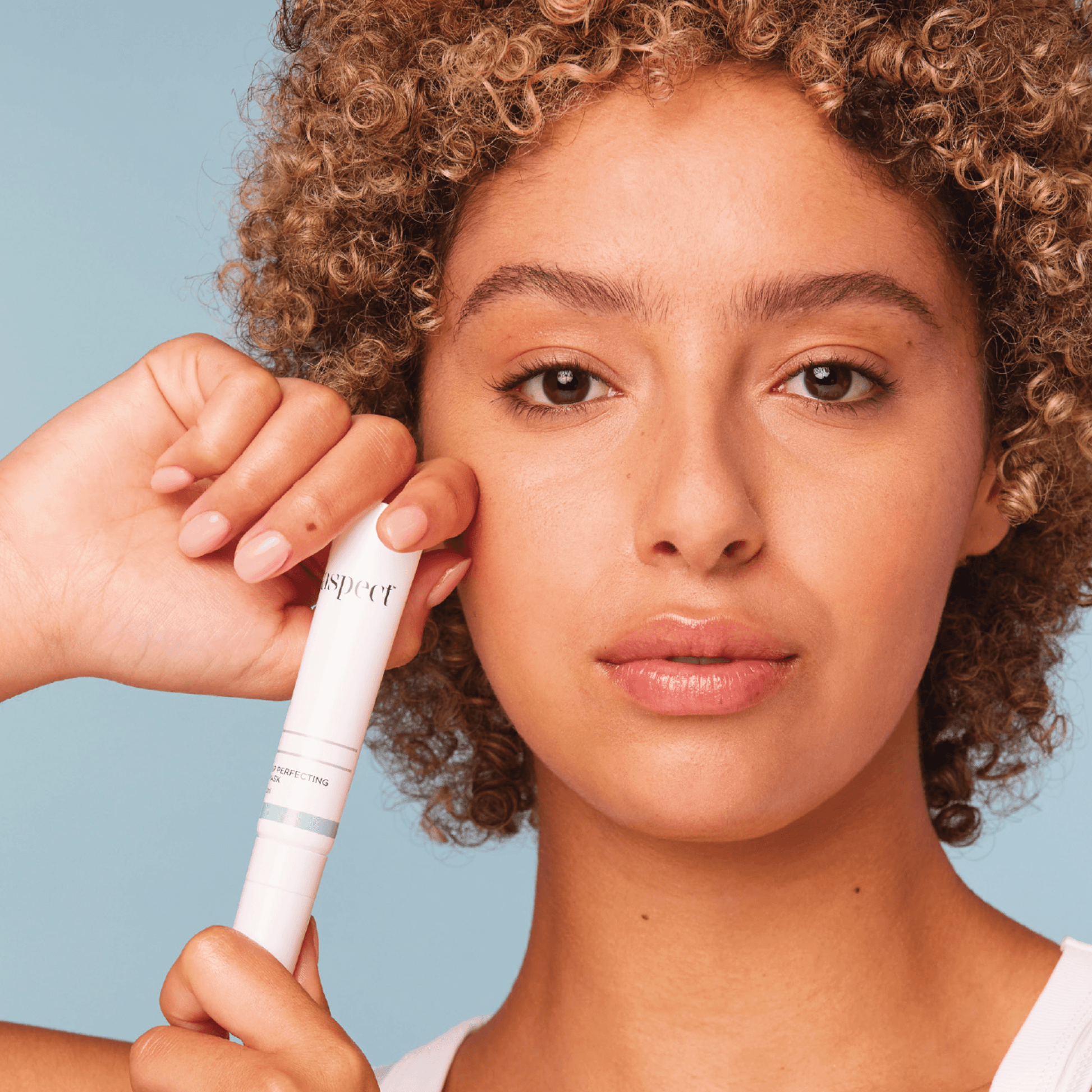 Woman holding an Aspect Lip Perfecting mask tube against a blue background