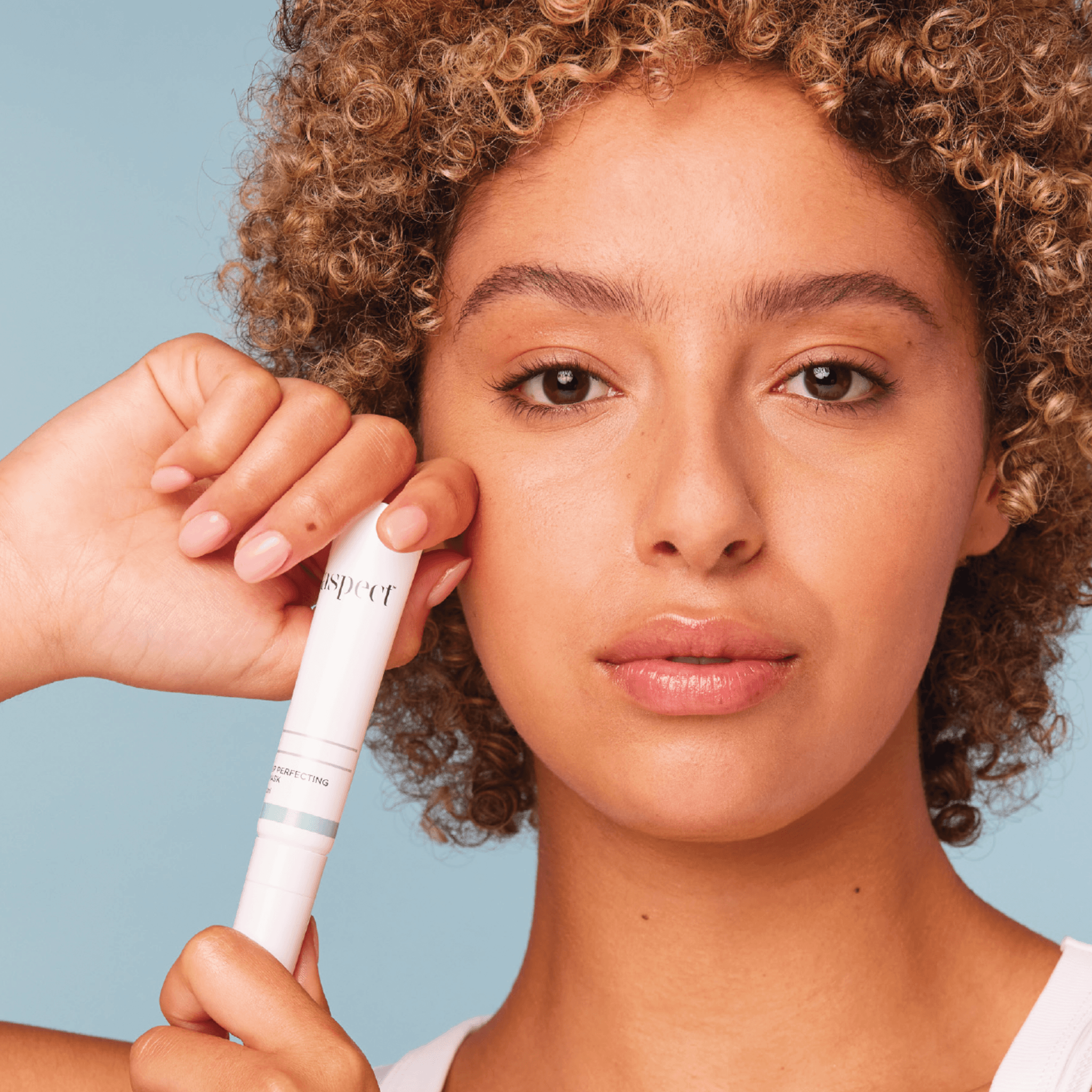 Woman holding an Aspect Lip Perfecting mask tube against a blue background