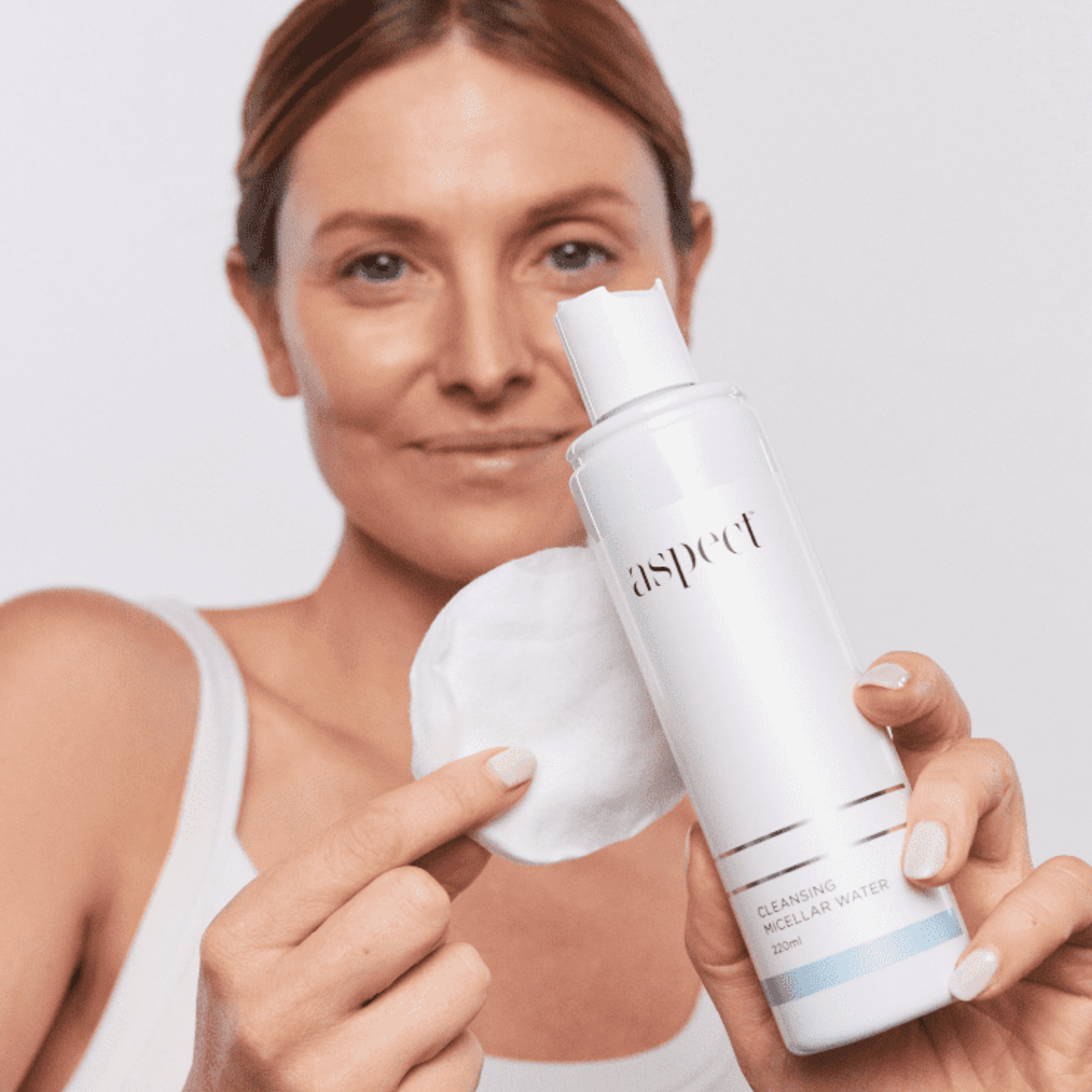 Woman holding a bottle of Aspect Cleansing Micellar water with a white background