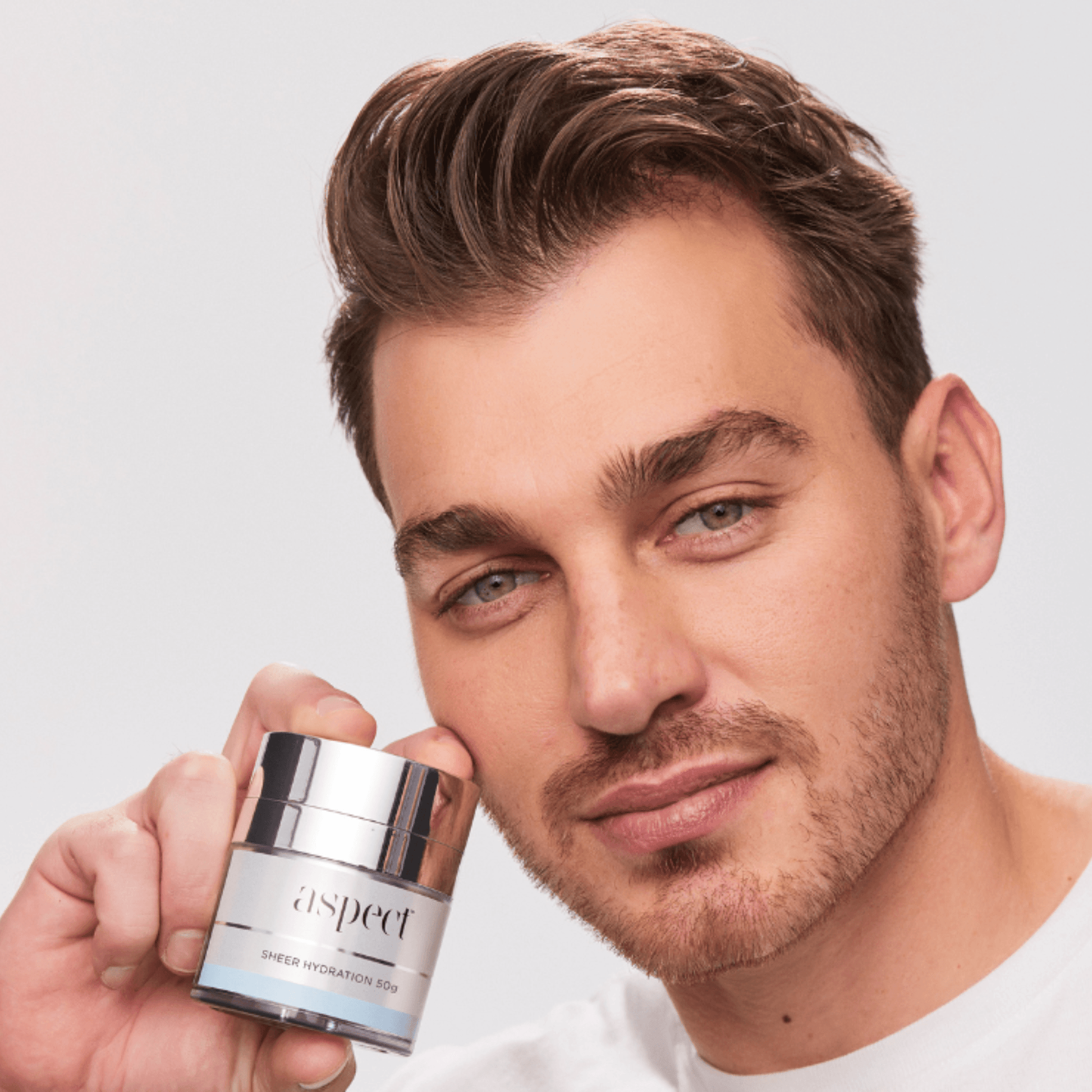 Man holding an Aspect Sheer Hydration Moisturiser against a plain background