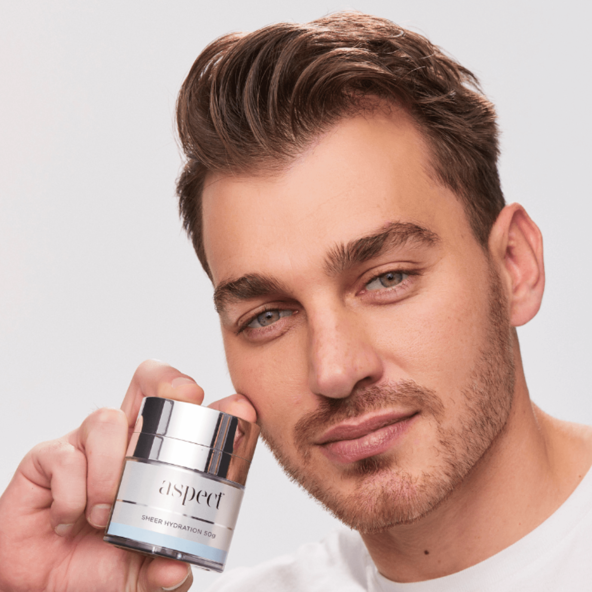 Man holding an Aspect Sheer Hydration Moisturiser against a plain background