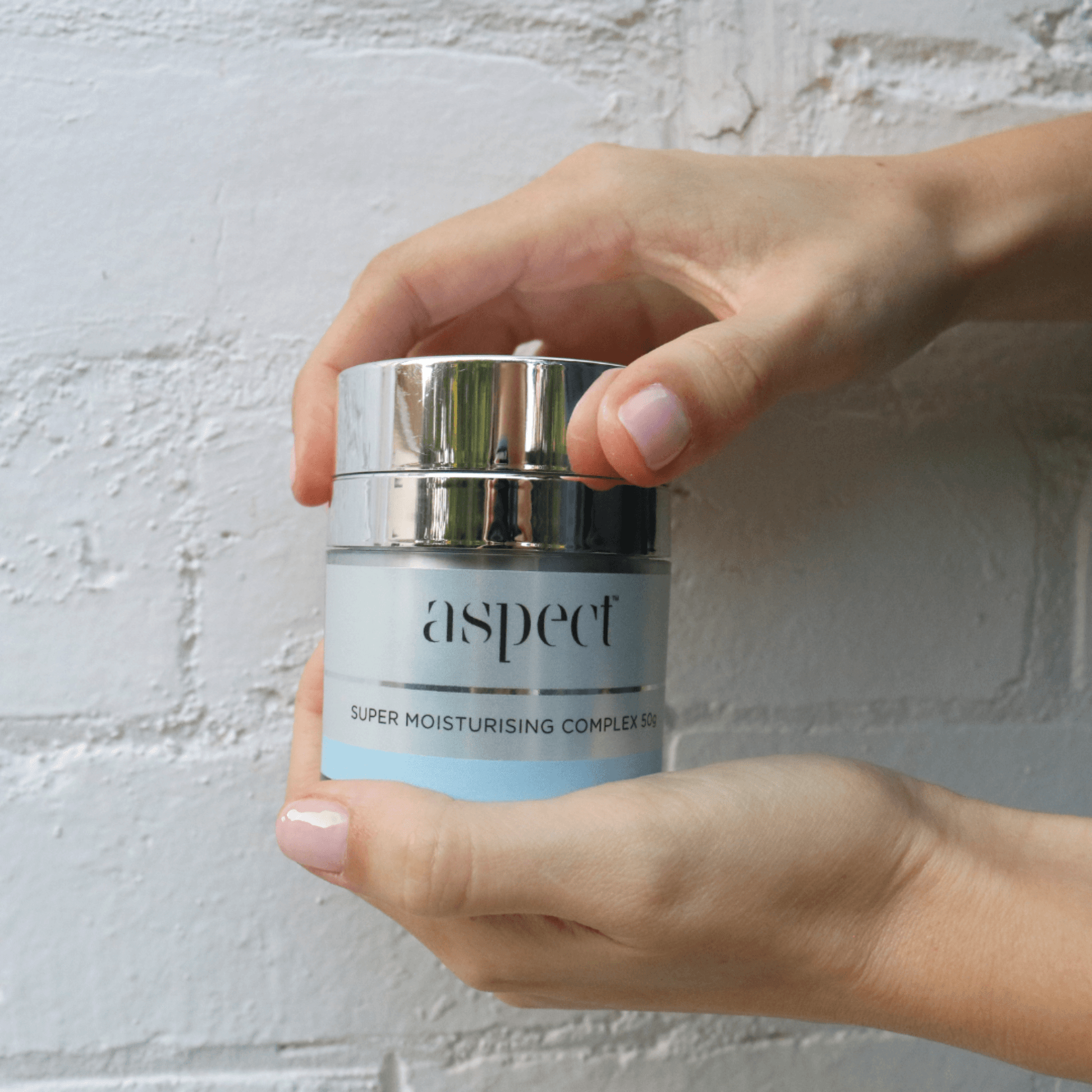 Hand holding a jar of 'aspect' super moisturising complex cream against a light background
