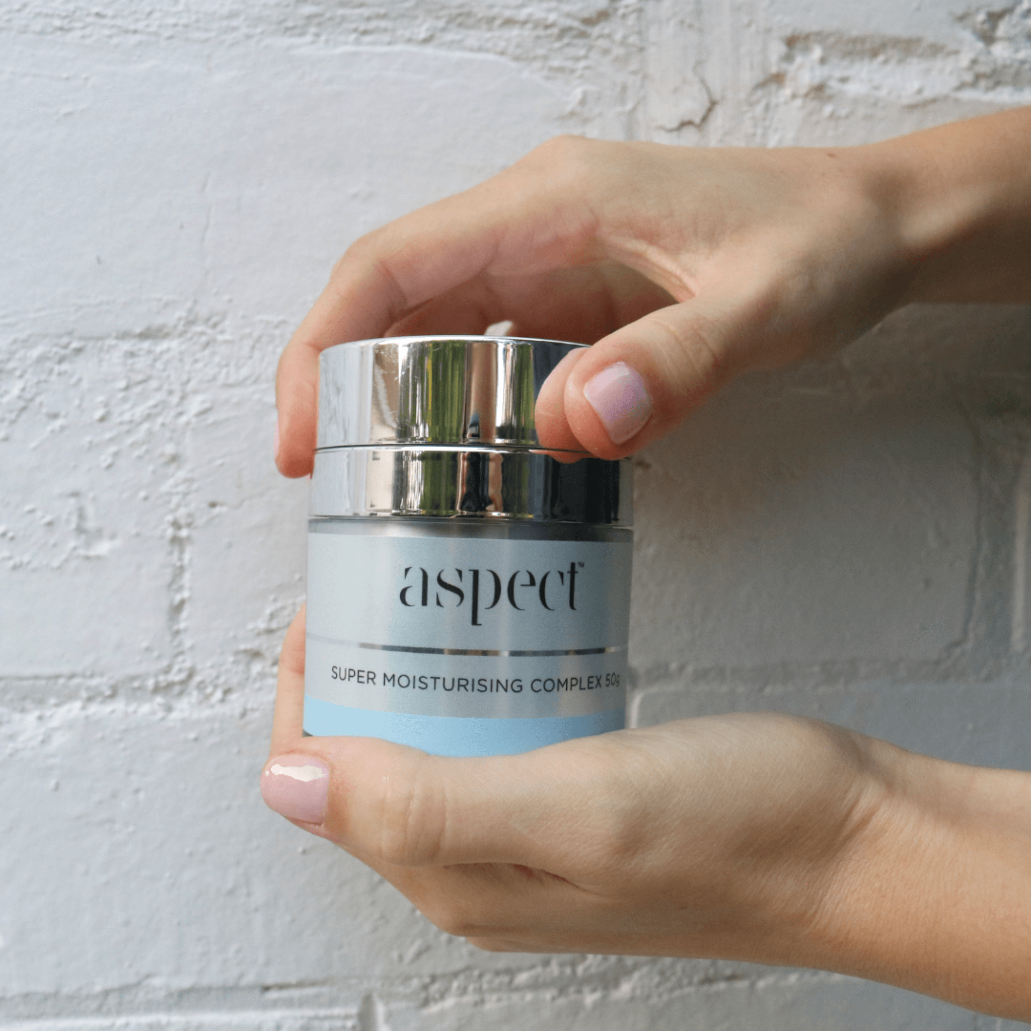 Hand holding a jar of 'aspect' super moisturising complex cream against a light background