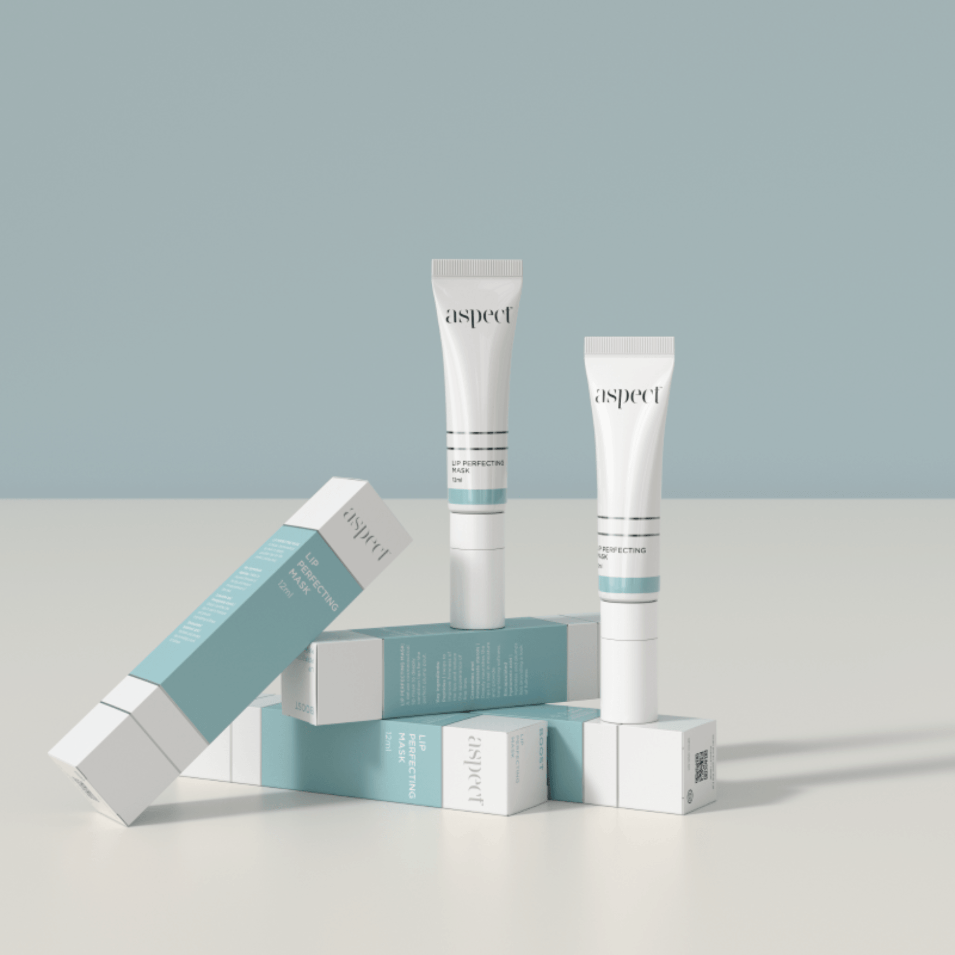 Two Aspect Lip Perfecting Mask tubes and their packaging on a light grey surface with a light blue background