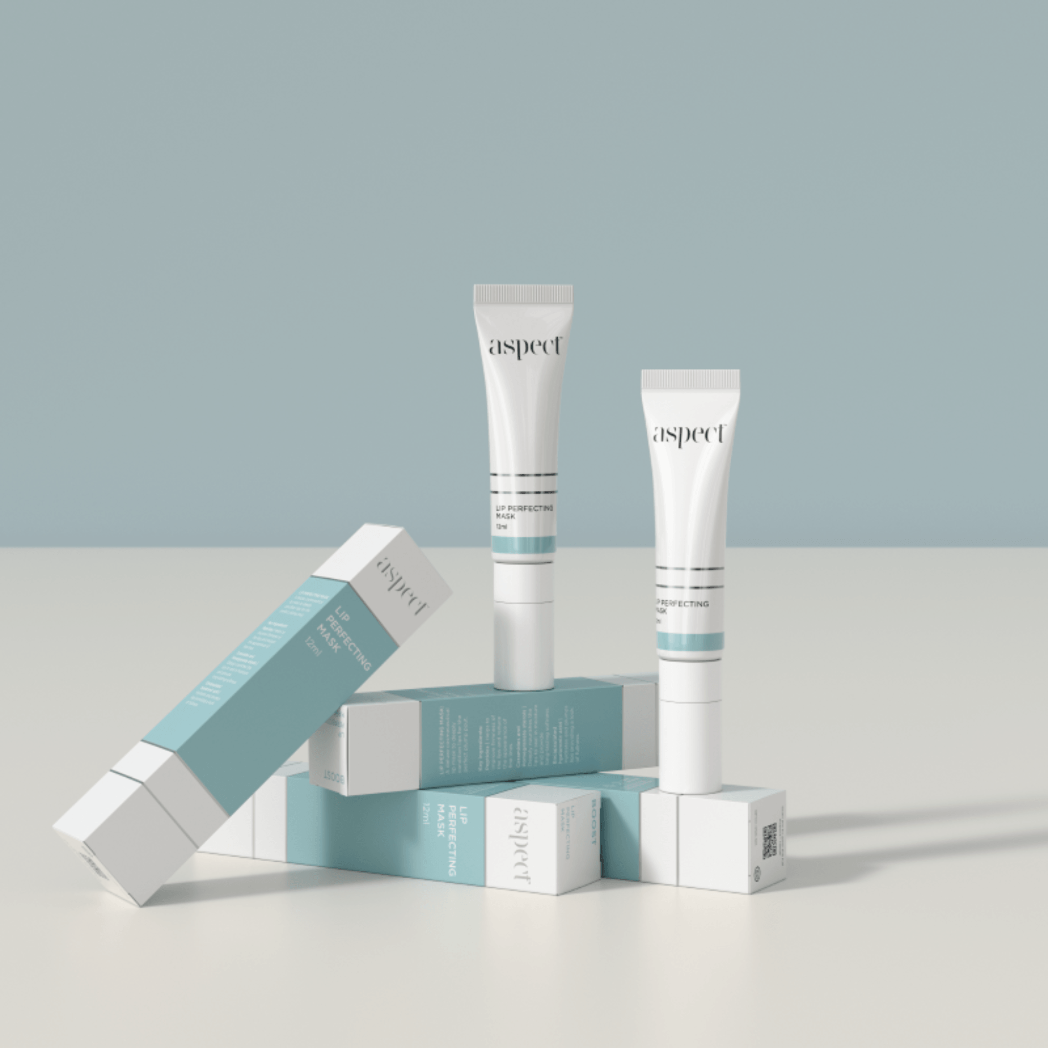 Two Aspect Lip Perfecting Mask tubes and their packaging on a light grey surface with a light blue background