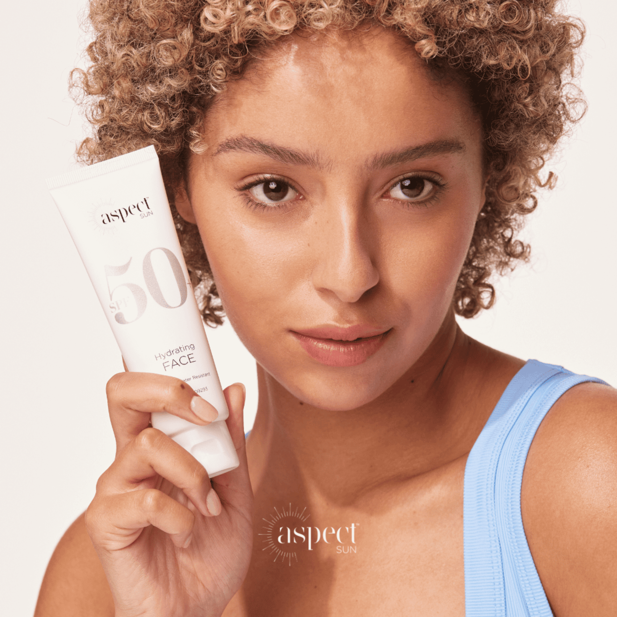 Woman holding a tube of Aspect Sun SPF50+ on a plain background
