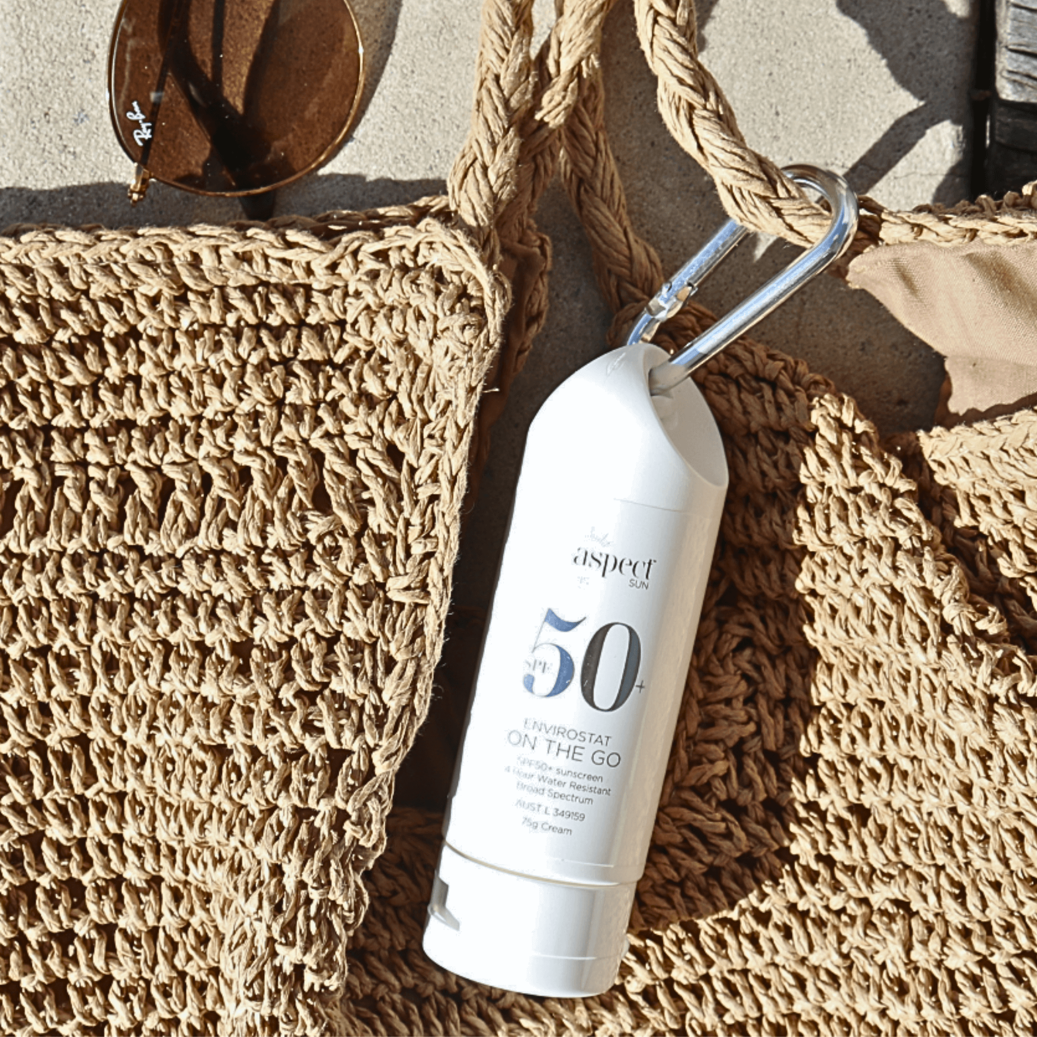 Sunscreen bottle labeled 'aspect sun' on a textured beach bag with sunglasses and cabana.