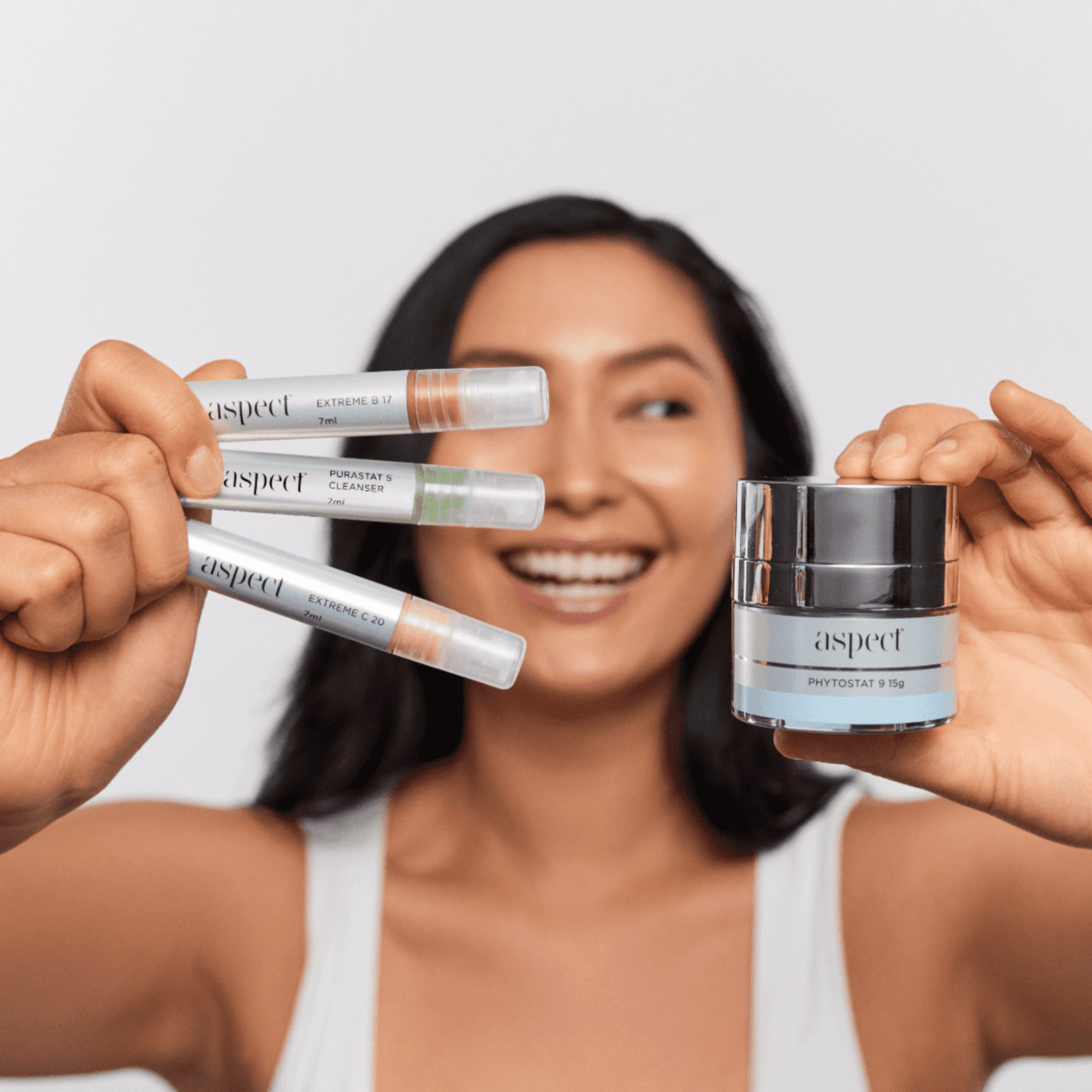 Woman holding Aspect Try Me Kit skincare products against a plain background