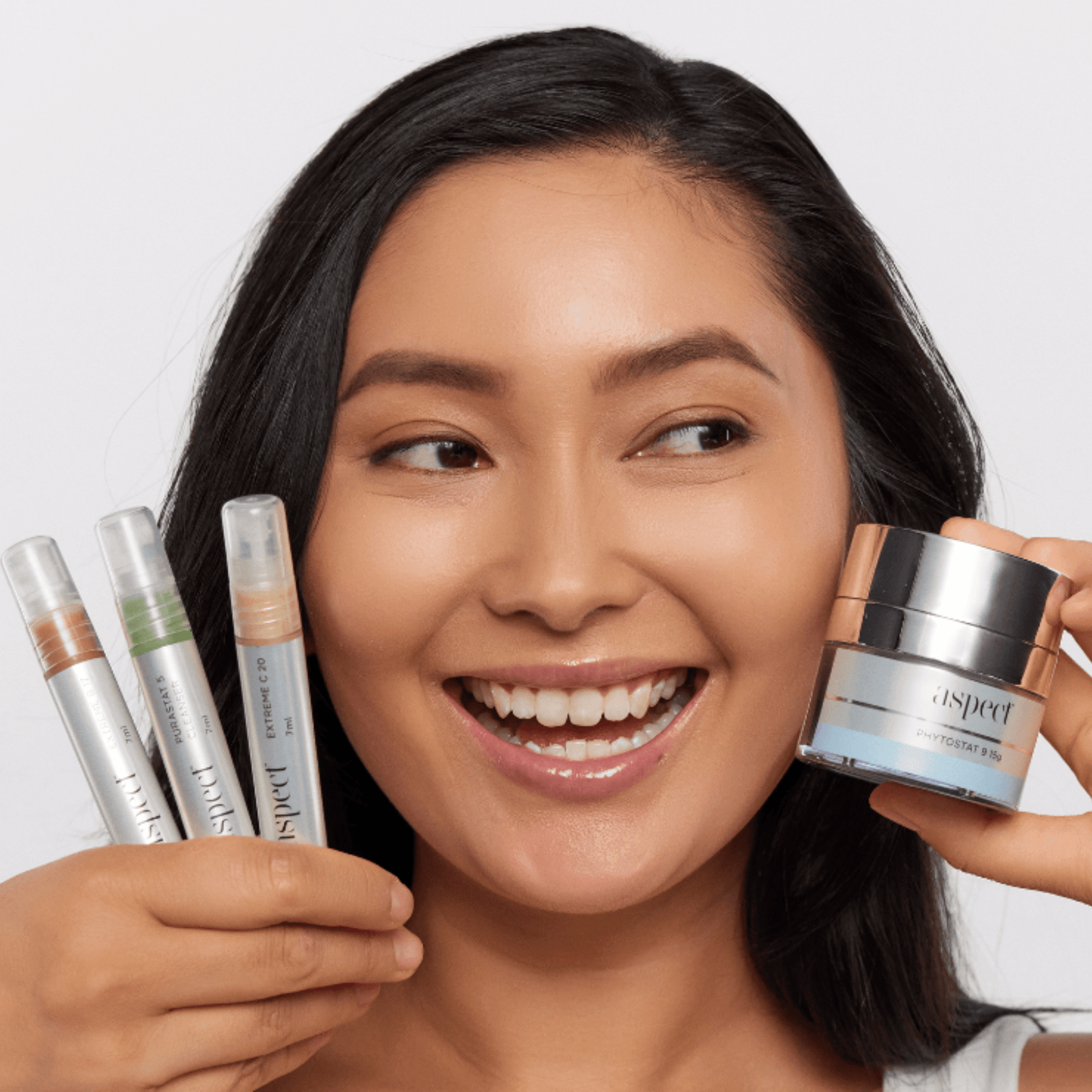 Woman holding Aspect skincare products including a jar and tubes on a white background