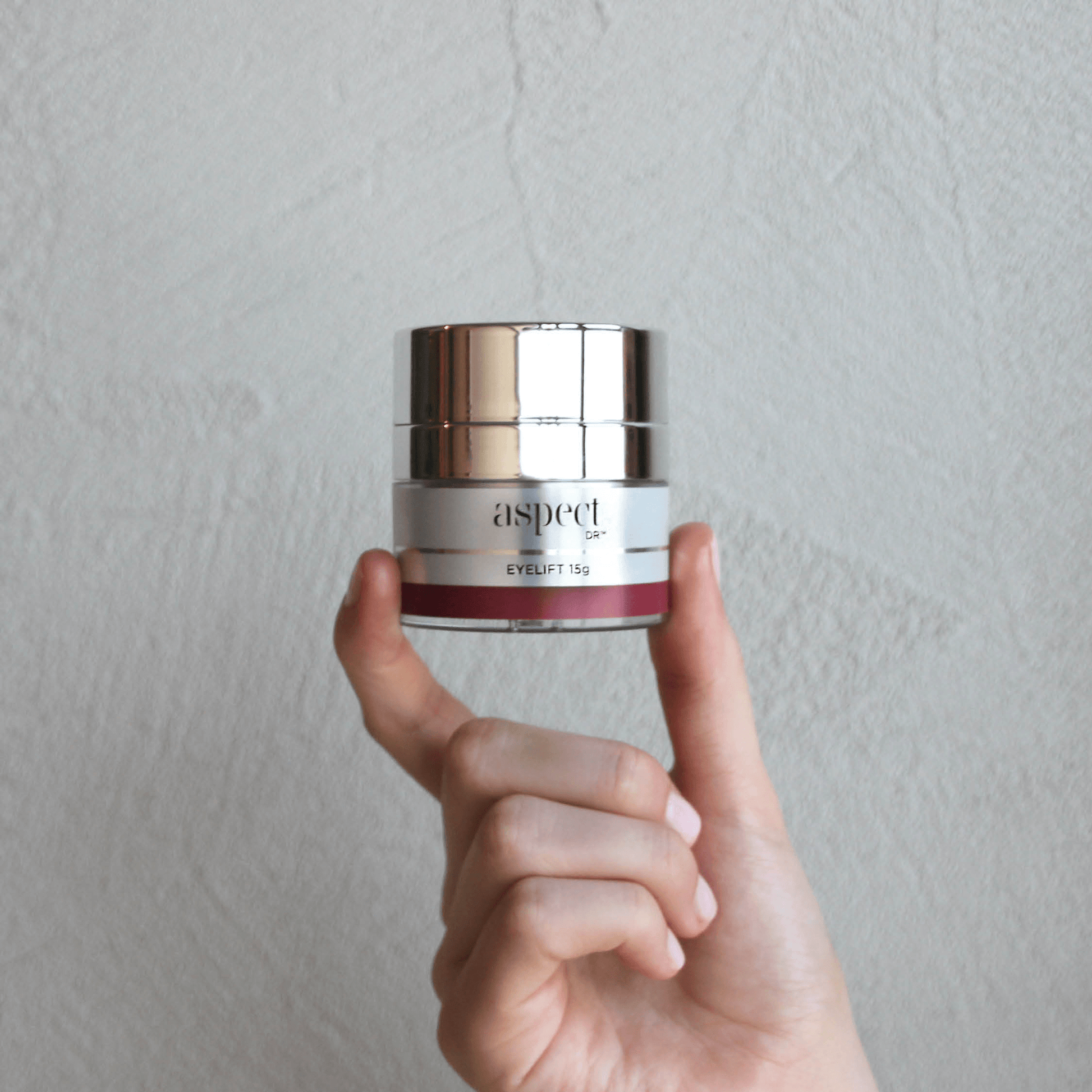 Aspect Eye Lift 15g jar being held near a textured background