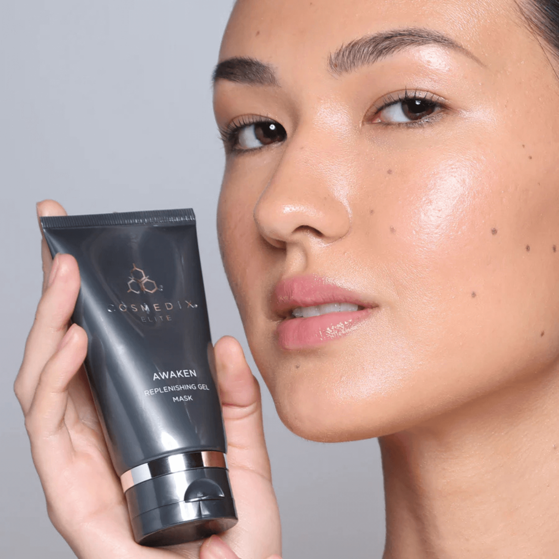 Model holding a Cosmedix Elite Awaken tube against a neutral background
