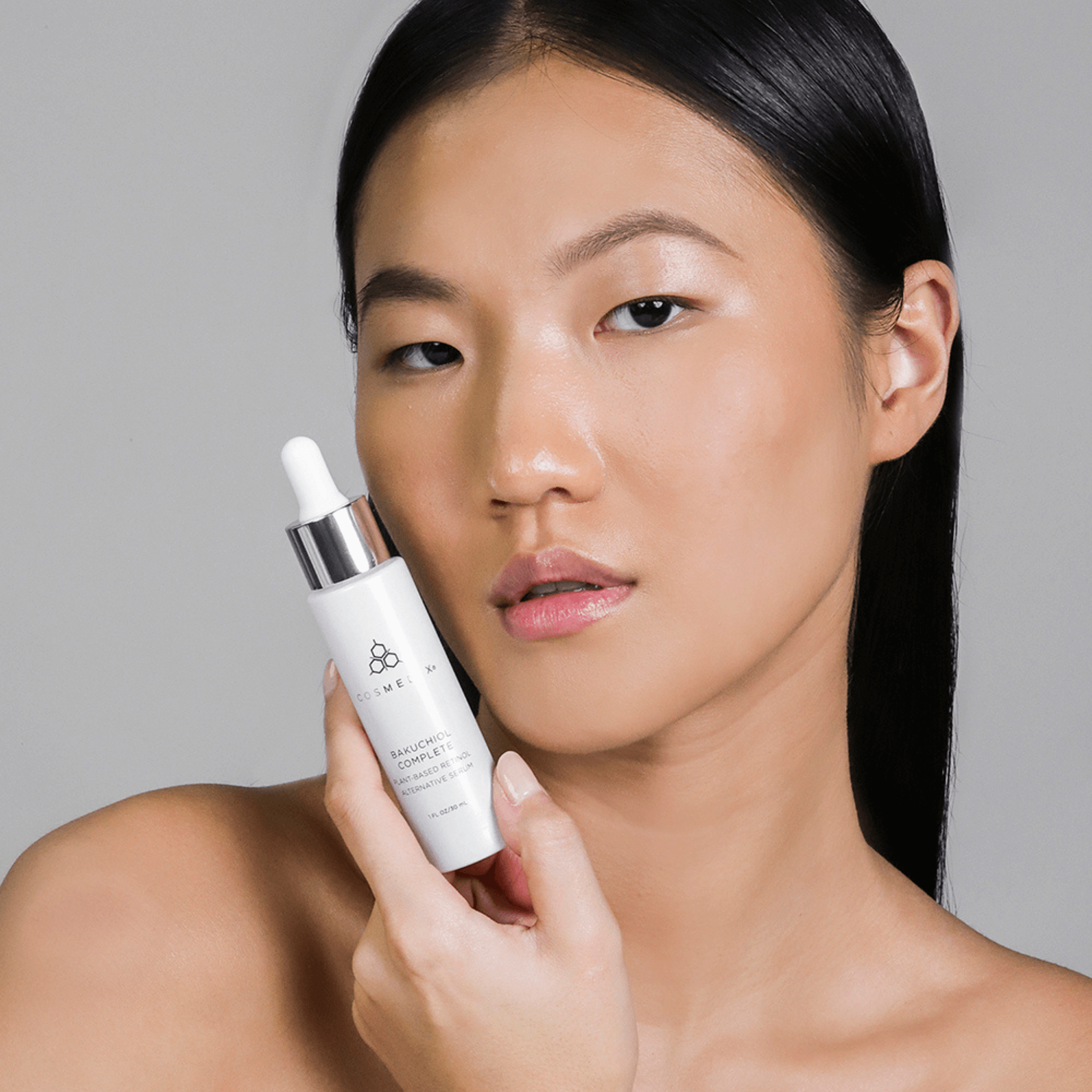 Woman holding Cosmedix Bakuchiol bottle against a neutral background