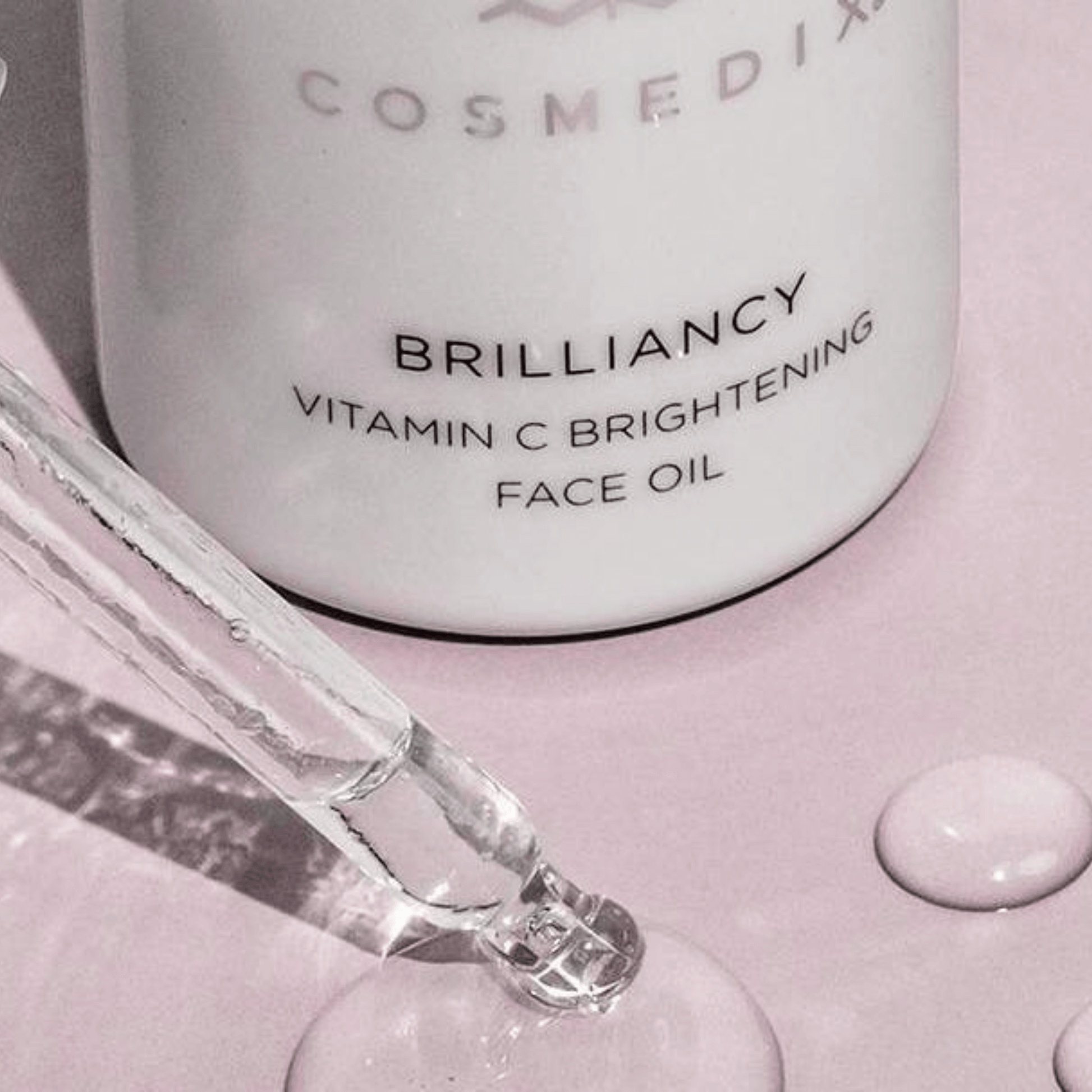 Cosmedix Brilliancy Vitamin C Brightening Face Oil with dropper on a pink background