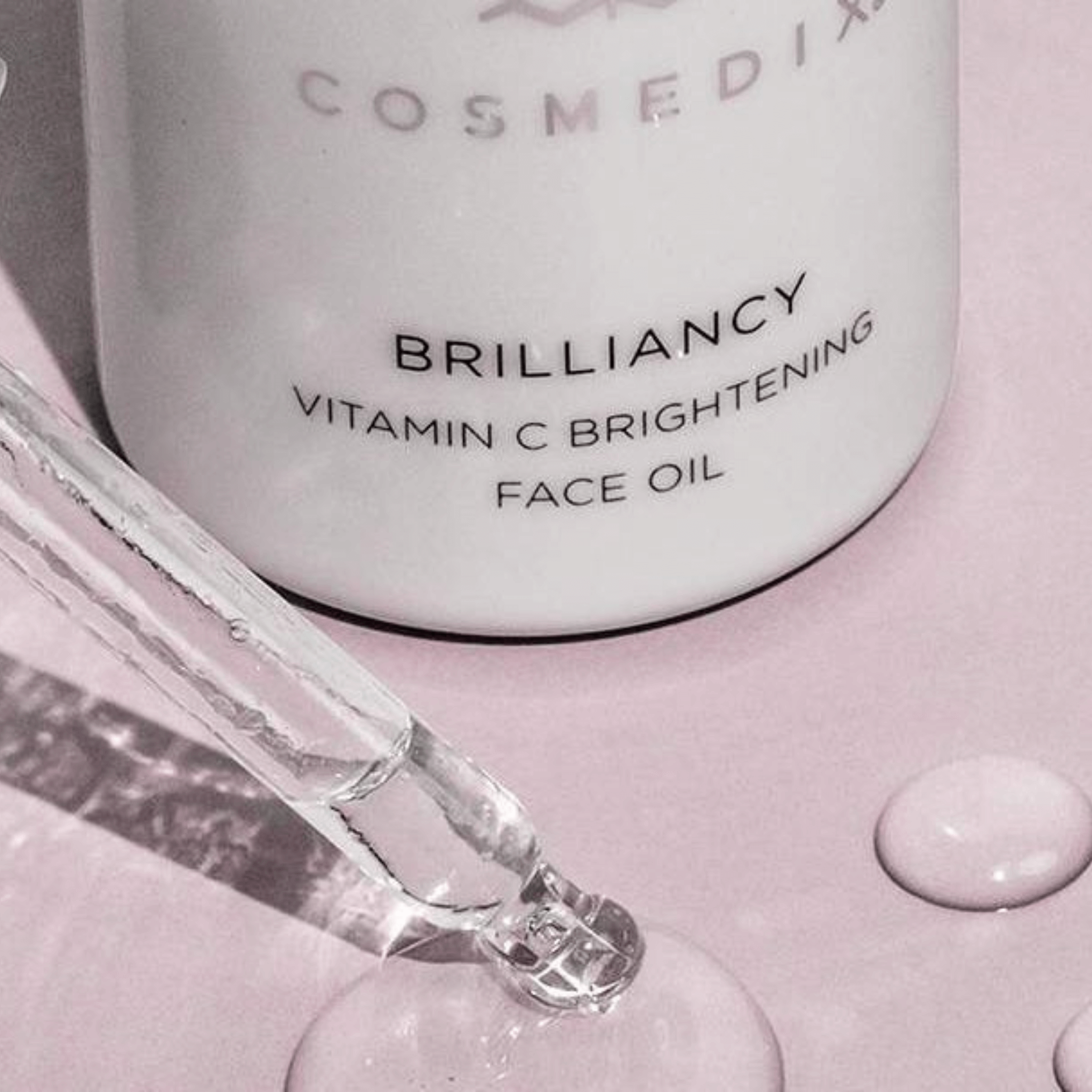 Cosmedix Brilliancy Vitamin C Brightening Face Oil with dropper on a pink background