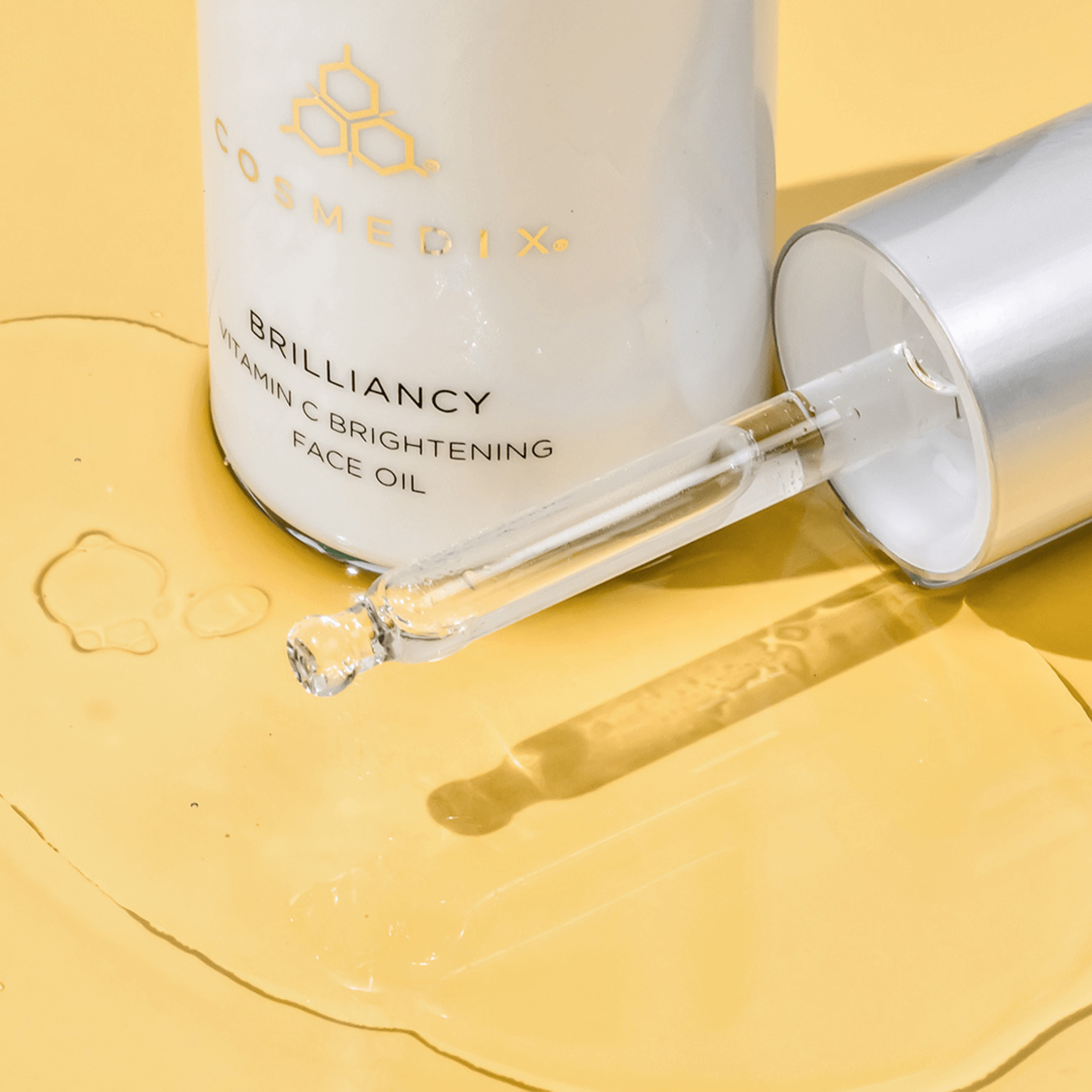 Cosmedix Brilliancy Vitamin C Brightening Face Oil with dropper on a yellow background