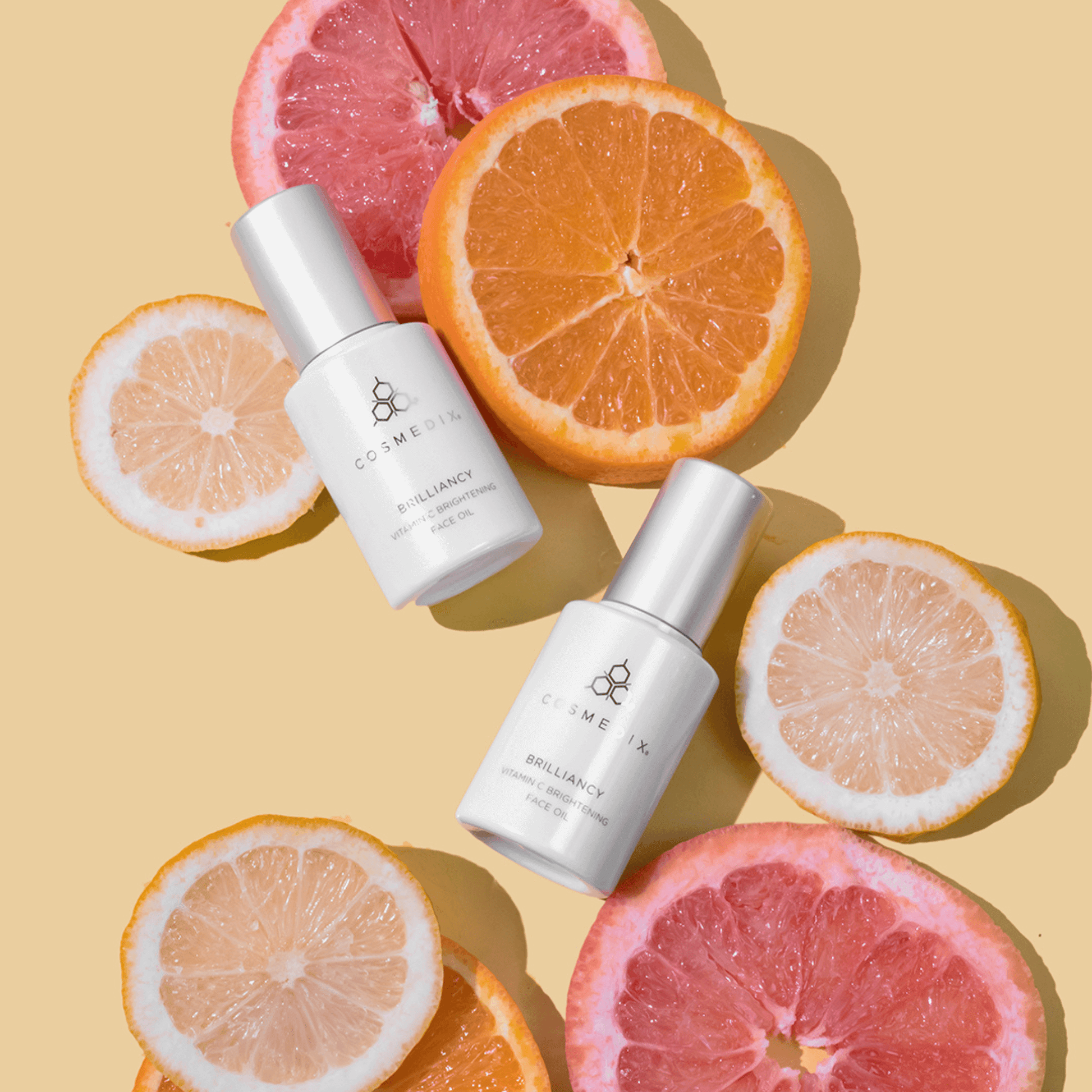 Two bottles of Cosmedix Brilliancy with citrus fruits on a beige background