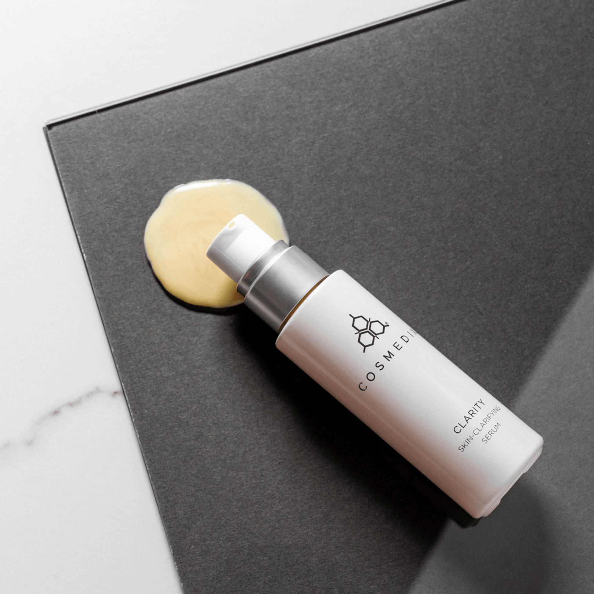 Cosmedix bottle labeled Clarity with a beige skincare sample on a dark surface