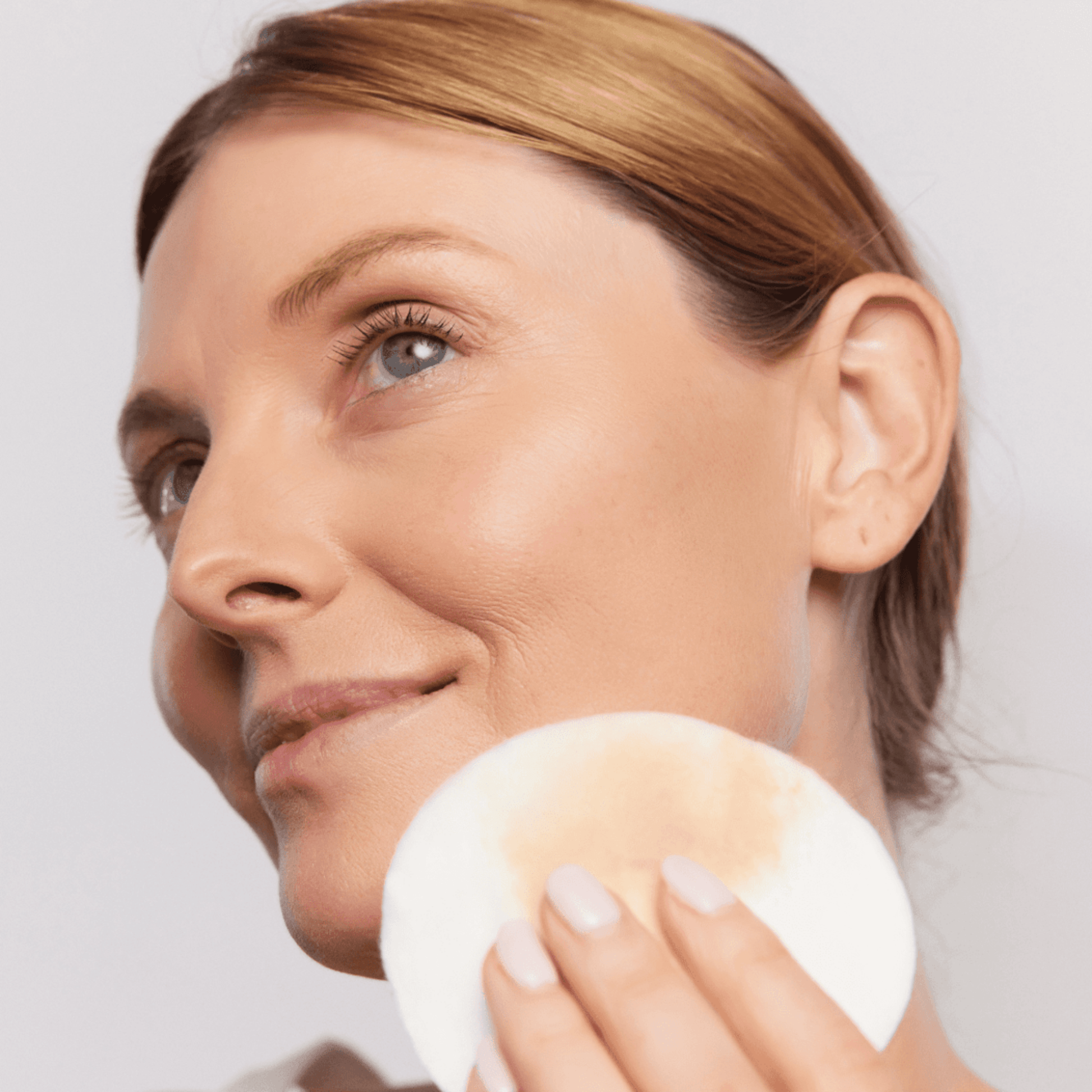 Woman holding a cotton pad with Aspect Micellar water against a plain background
