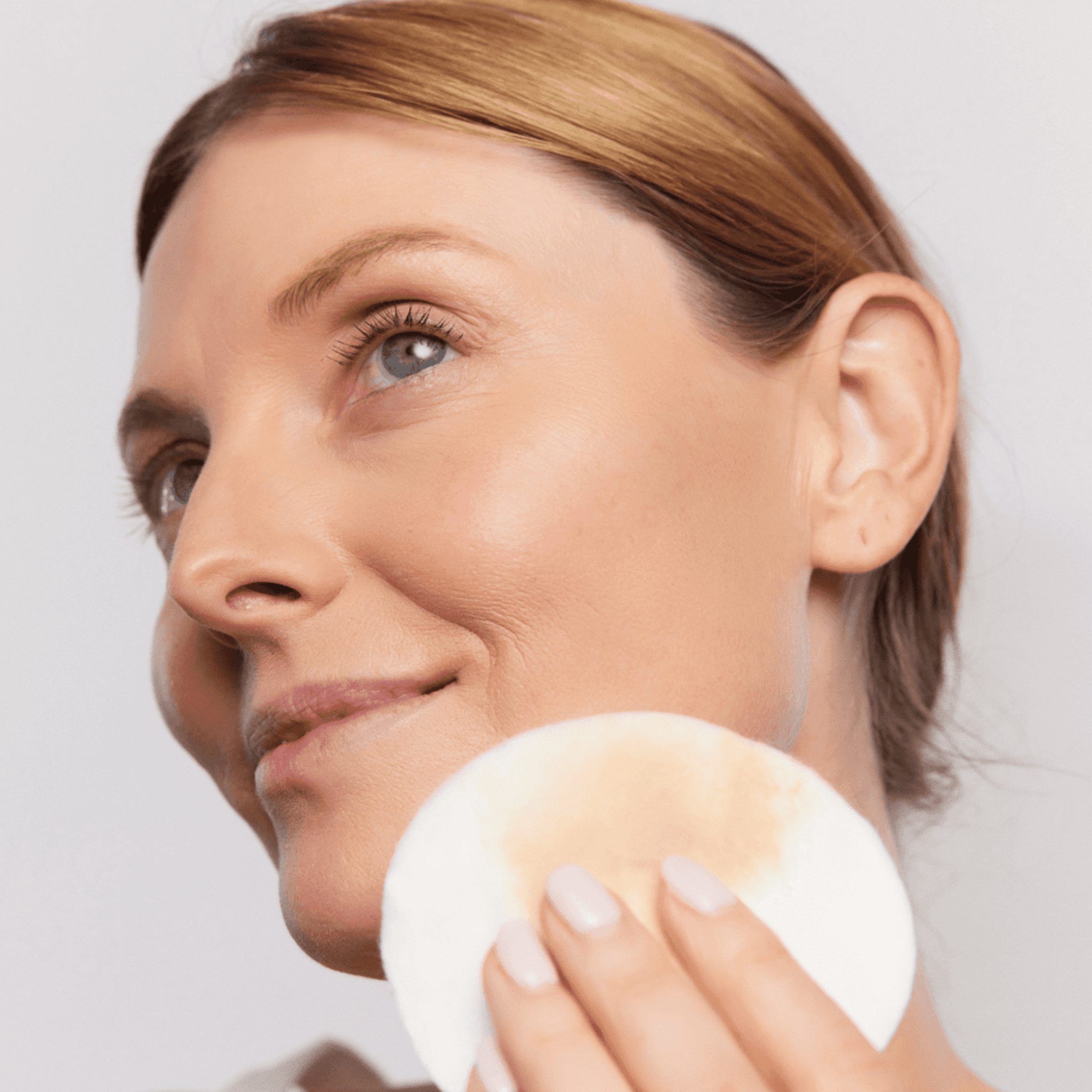 Woman holding a cotton pad with Aspect Micellar water against a plain background