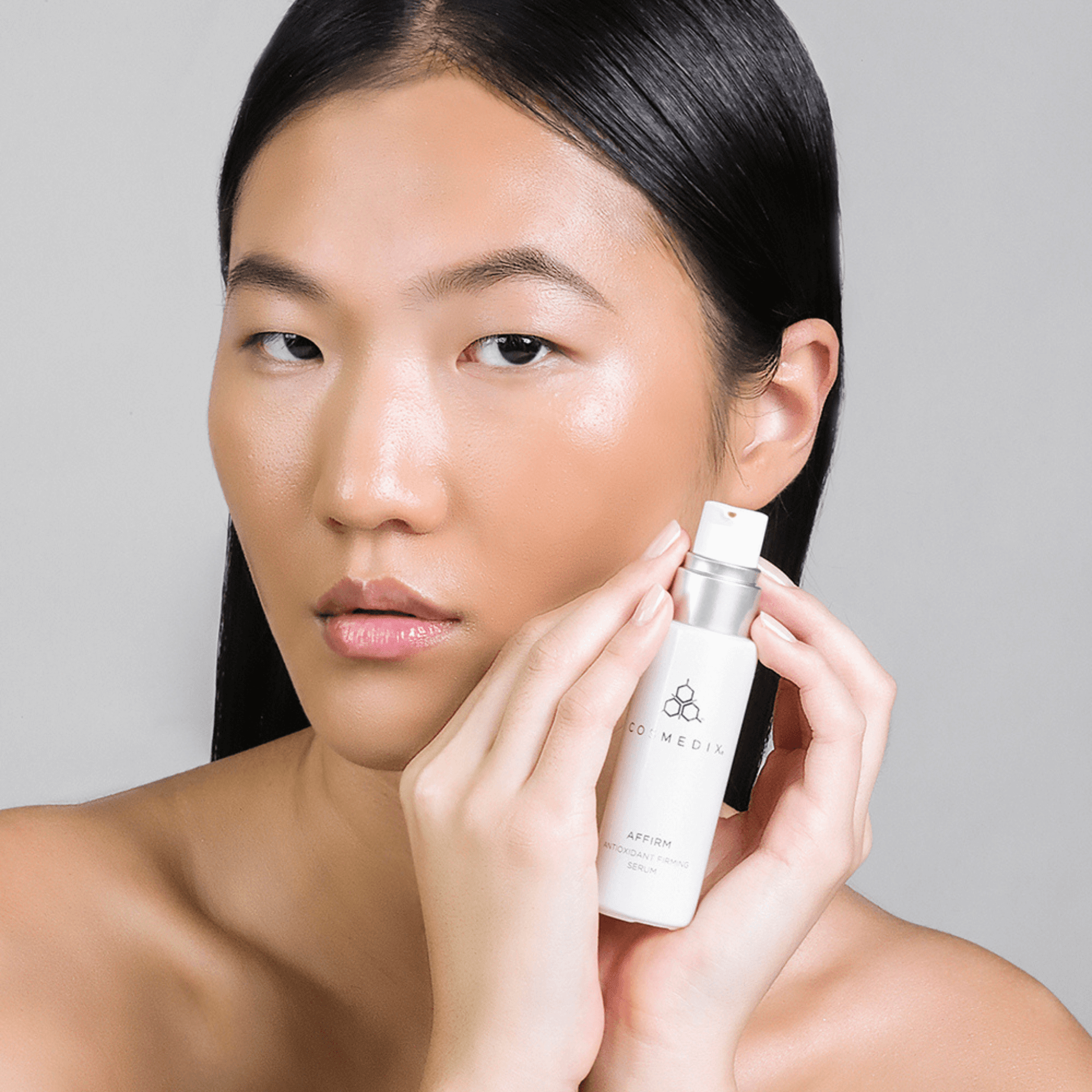 Woman holding Cosmedix Affirm bottle on light grey background