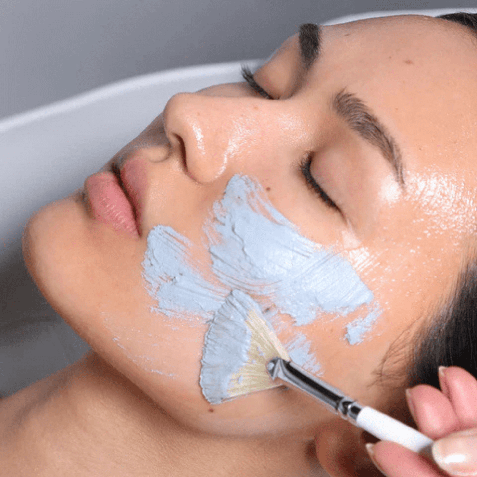 Person applying Cosmedix Detox Activated Charcoal Mask with a brush to their face