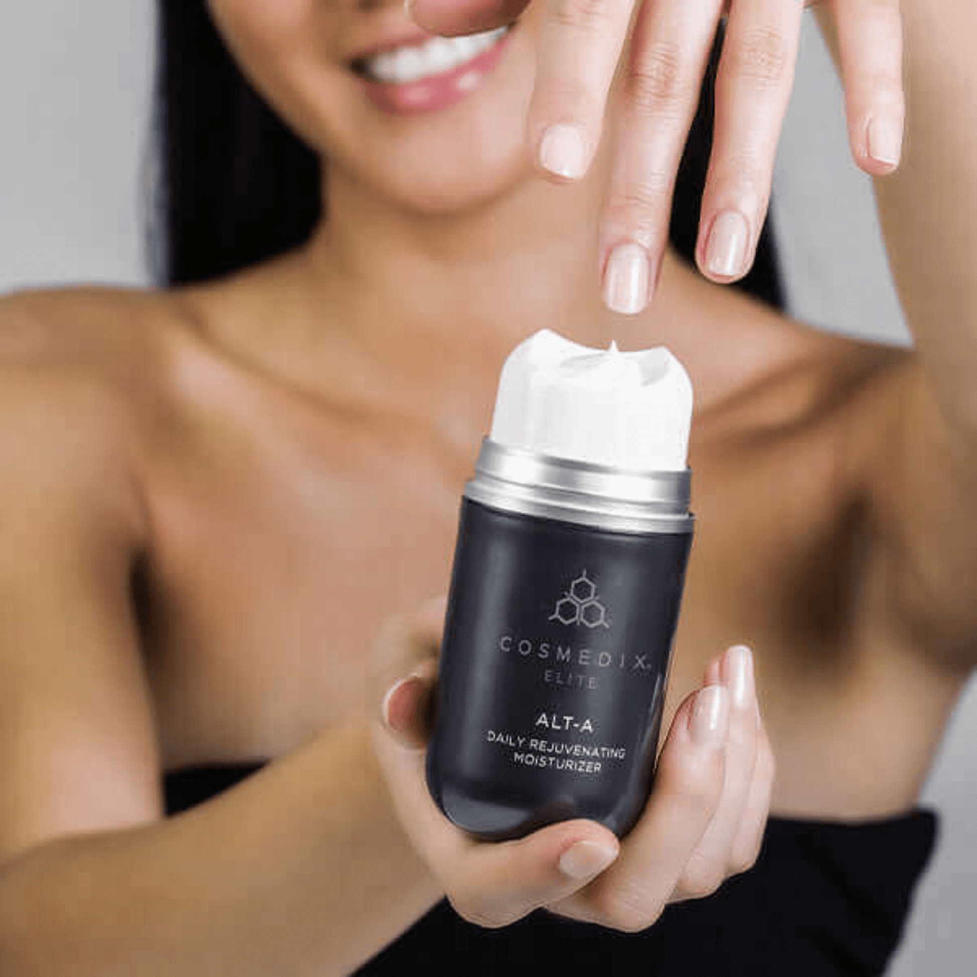 Woman holding a Cosmedix Elite Alt-A moisturiser skincare product with a blurred background