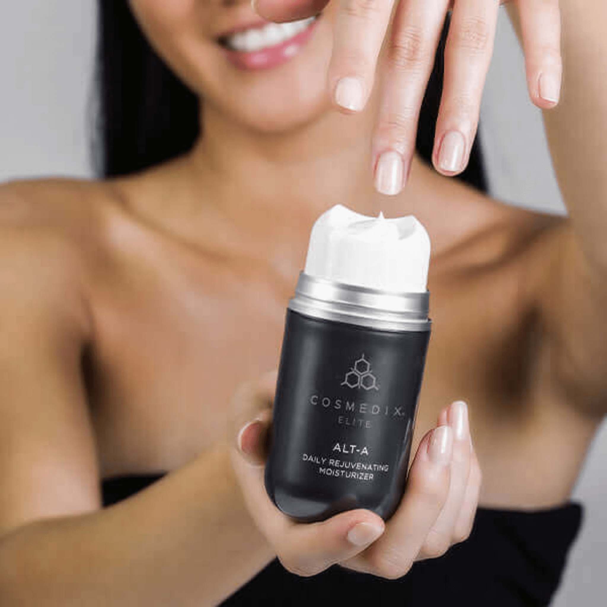Woman holding a Cosmedix Elite Alt-A moisturiser skincare product with a blurred background